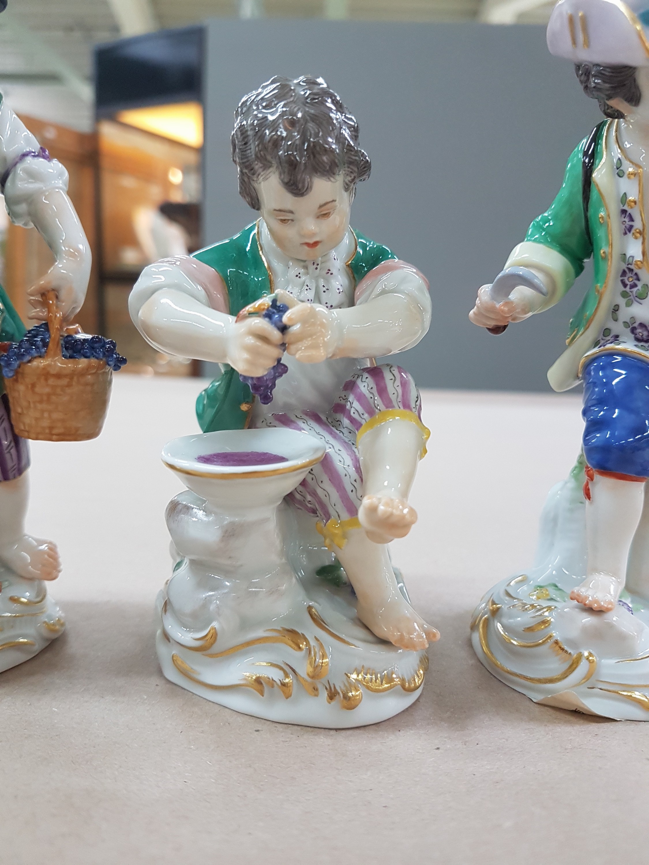 Detail c: 3 Porzellanfiguren, Meissen, 20. Jh., 1. Wahl, 3 Winzerknaben mit roten Trauben in Kiepe, Korb und beim Auspressen, H. ca. 11-14 cm