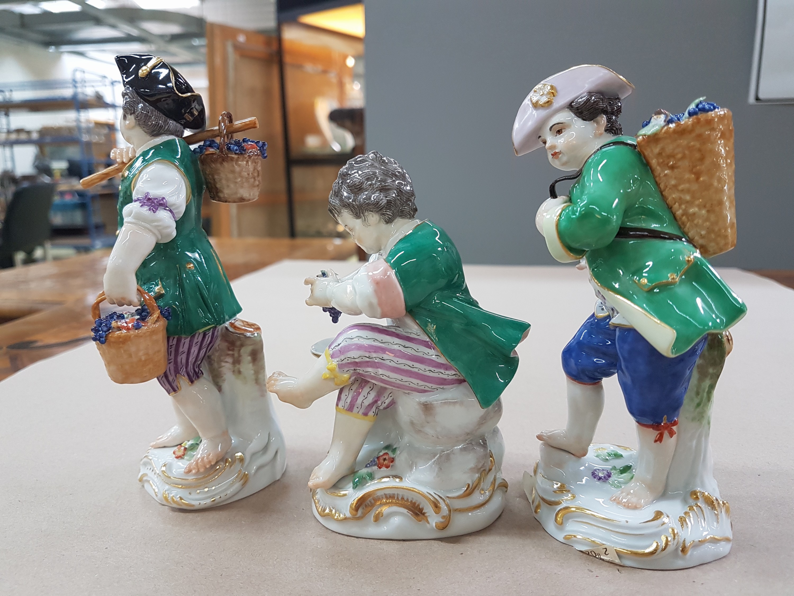 Detail e: 3 Porzellanfiguren, Meissen, 20. Jh., 1. Wahl, 3 Winzerknaben mit roten Trauben in Kiepe, Korb und beim Auspressen, H. ca. 11-14 cm