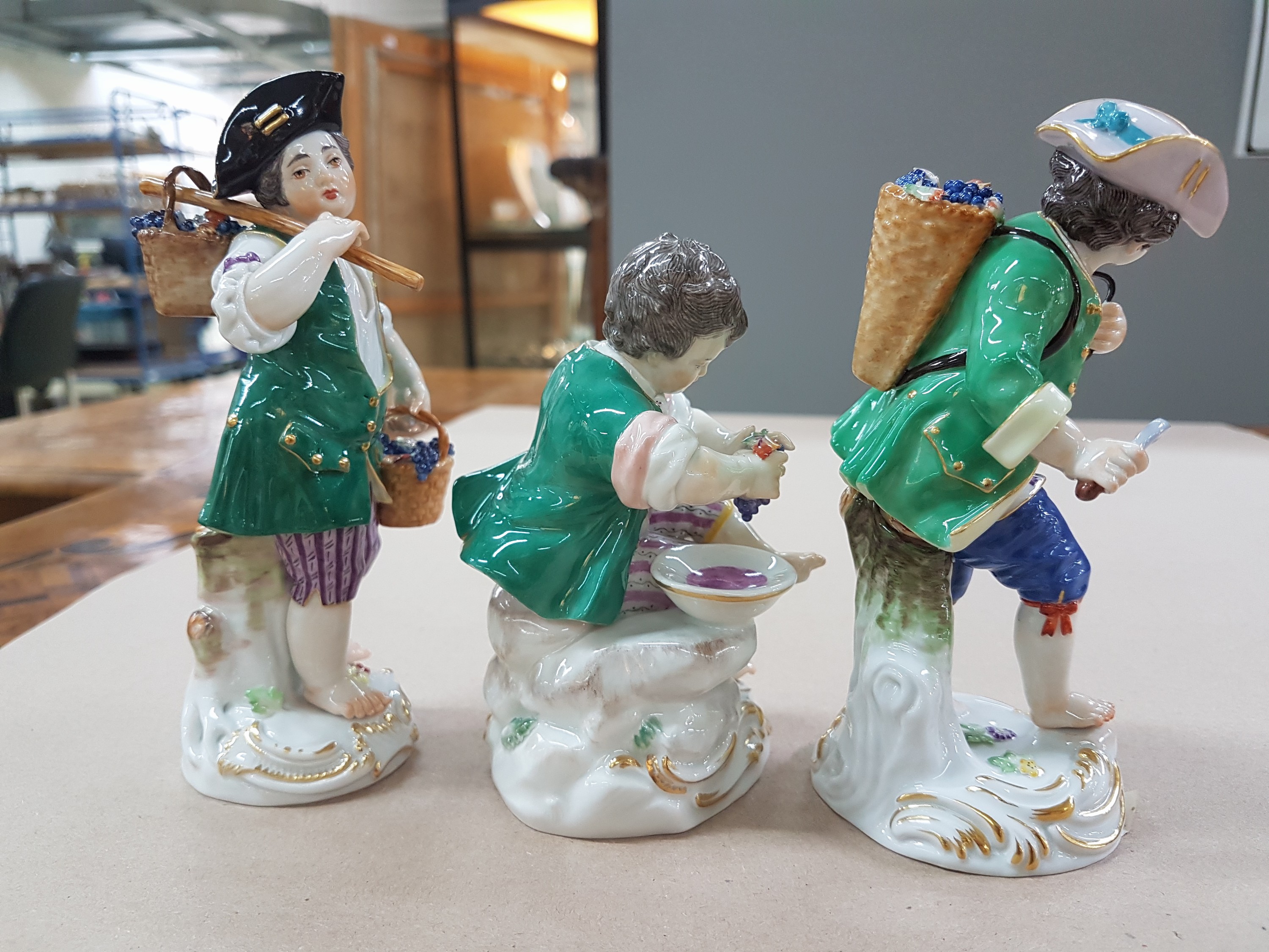 Detail g: 3 Porzellanfiguren, Meissen, 20. Jh., 1. Wahl, 3 Winzerknaben mit roten Trauben in Kiepe, Korb und beim Auspressen, H. ca. 11-14 cm