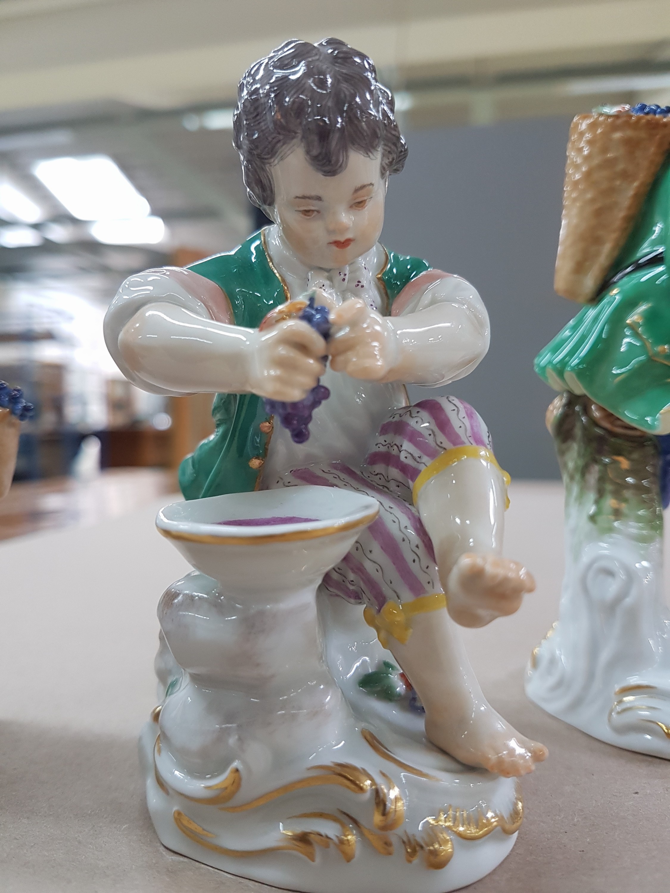 Detail i: 3 Porzellanfiguren, Meissen, 20. Jh., 1. Wahl, 3 Winzerknaben mit roten Trauben in Kiepe, Korb und beim Auspressen, H. ca. 11-14 cm