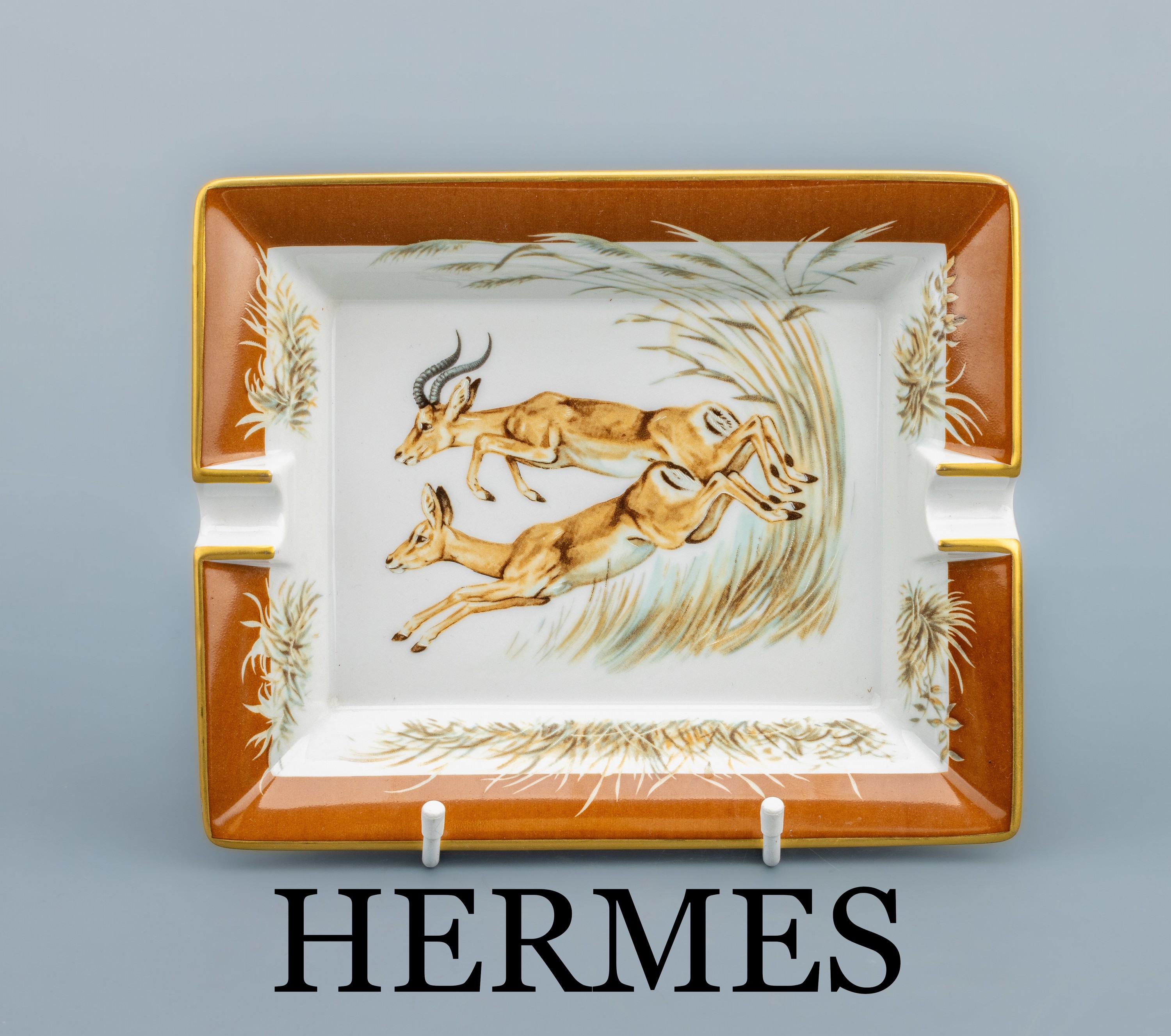 HERMES Aschenbecher, Porzellan, weißer Fondmit Springböcken, Fahne braun mit Goldrand, Boden mit braunem Velourleder, ca. 20 x 16.5 cm, sign.