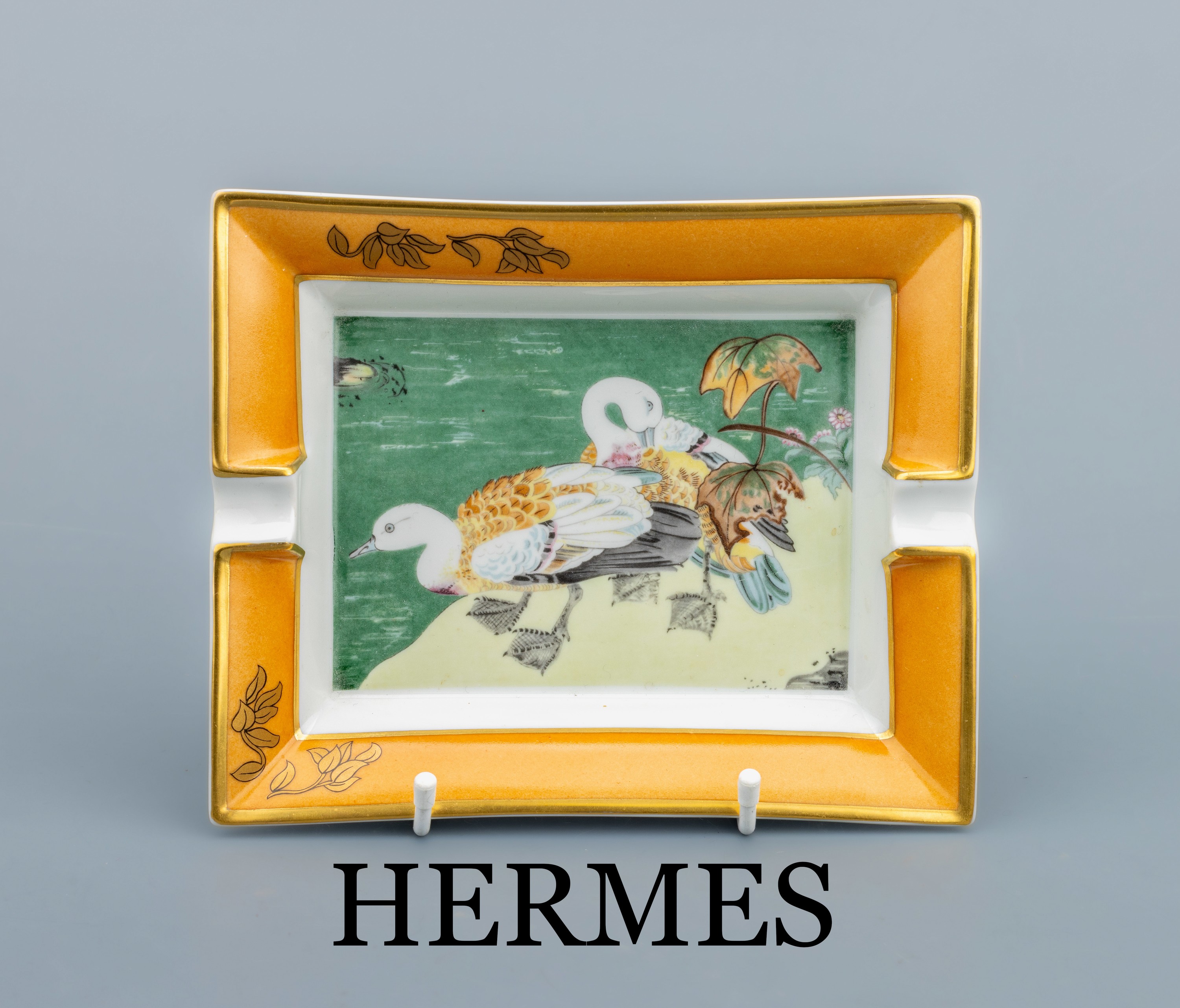 HERMES Aschenbecher, weißer Fond mit Enten an See, Fahne braun mit Blättern, Goldrand, Boden mit Velourleder, ca. 19.5 x 16 cm, sign.