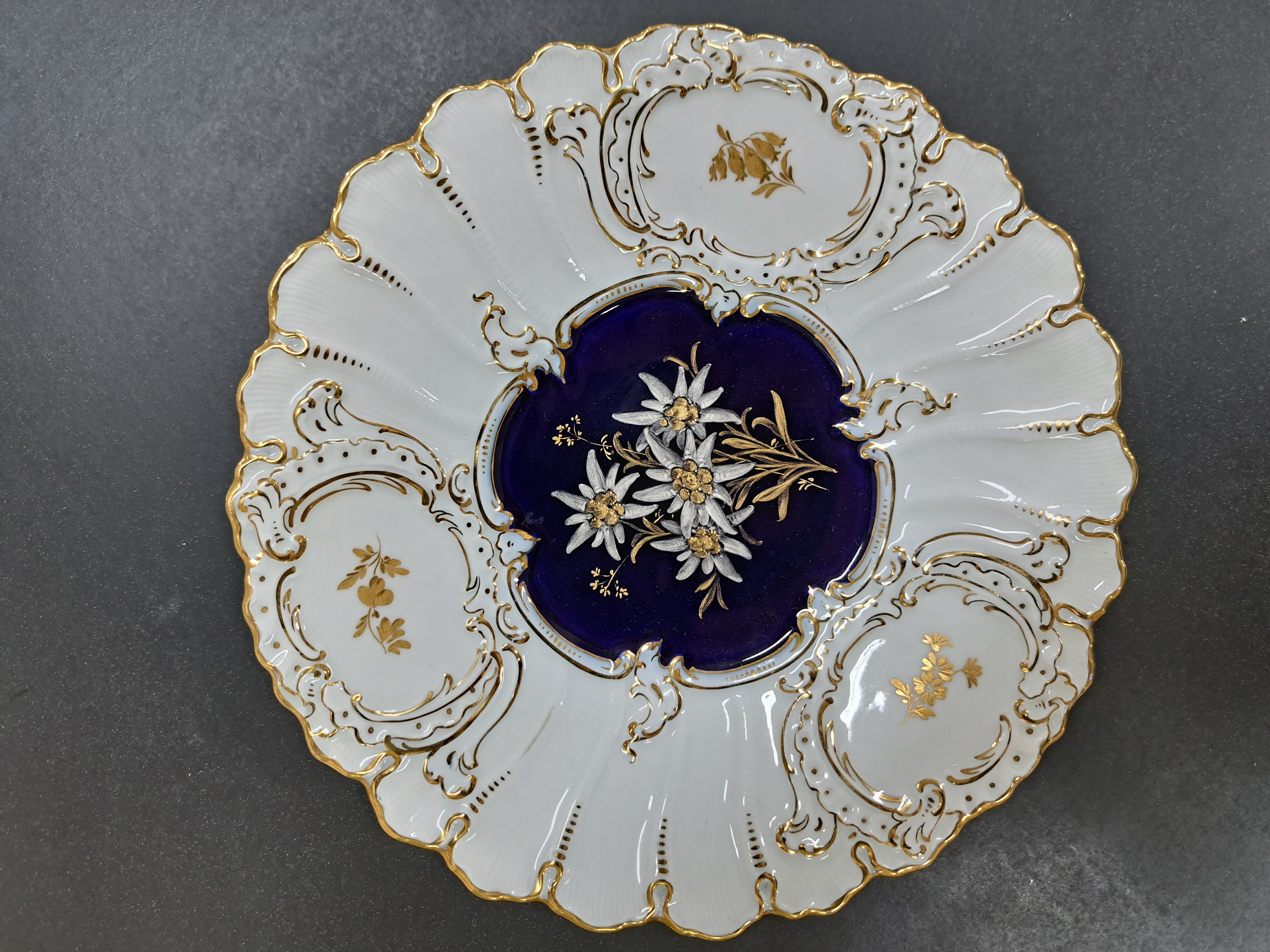 Detail a: Prunkteller, Meissen, Pfeifferzeit um 1924-33, 1. Wahl, reliefiert und reich glanzvergoldet, mittig Dekor von Edelweiß auf kobaltblauem Grund, D. ...