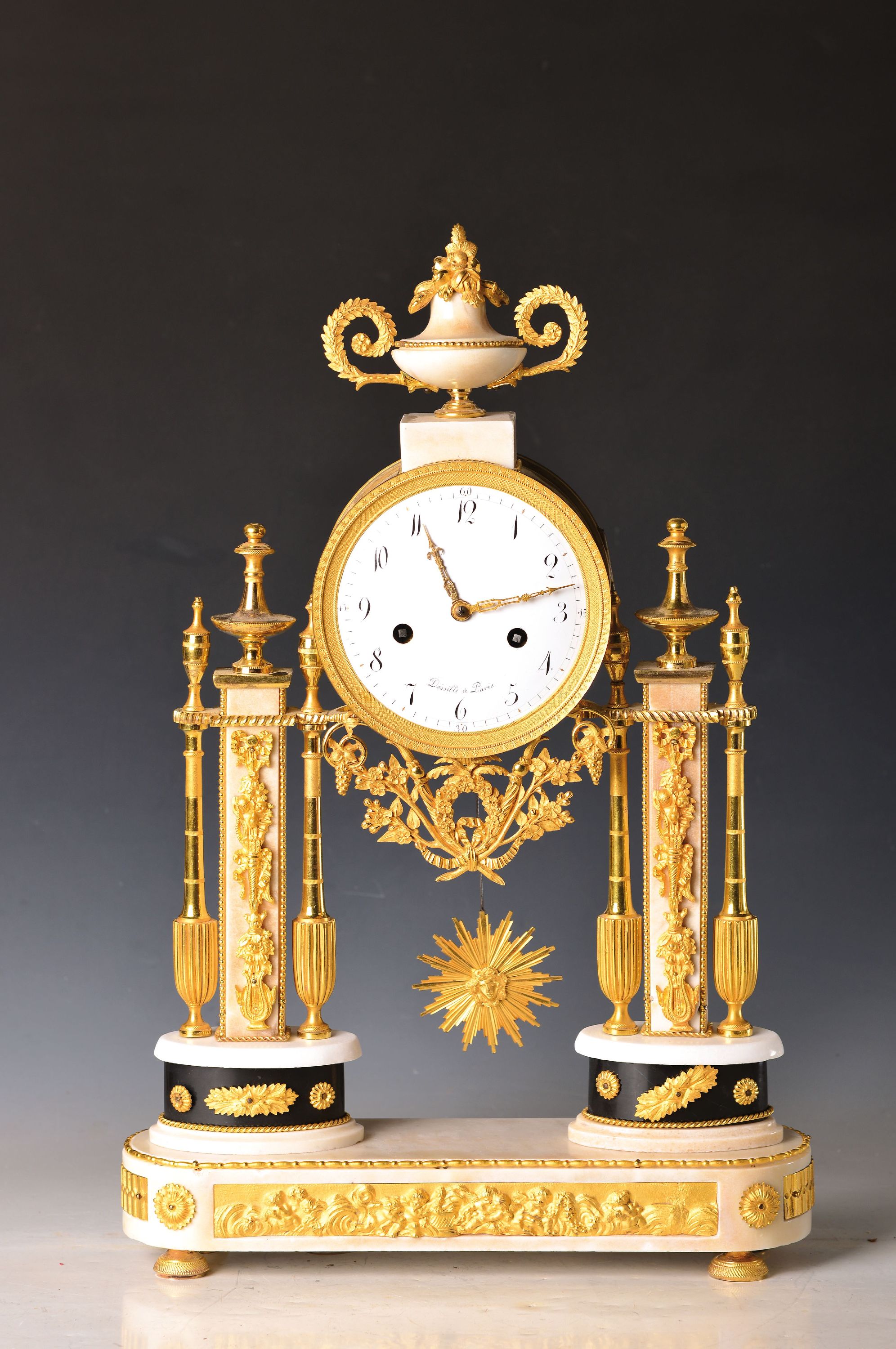 Detail a: Portaluhr, Dessille a Paris, um 1790, feuervergoldete Appliken auf weißem Marmor, Sockel mit reliefierten Putti, darauf zwei ovale Plinthen mit ...