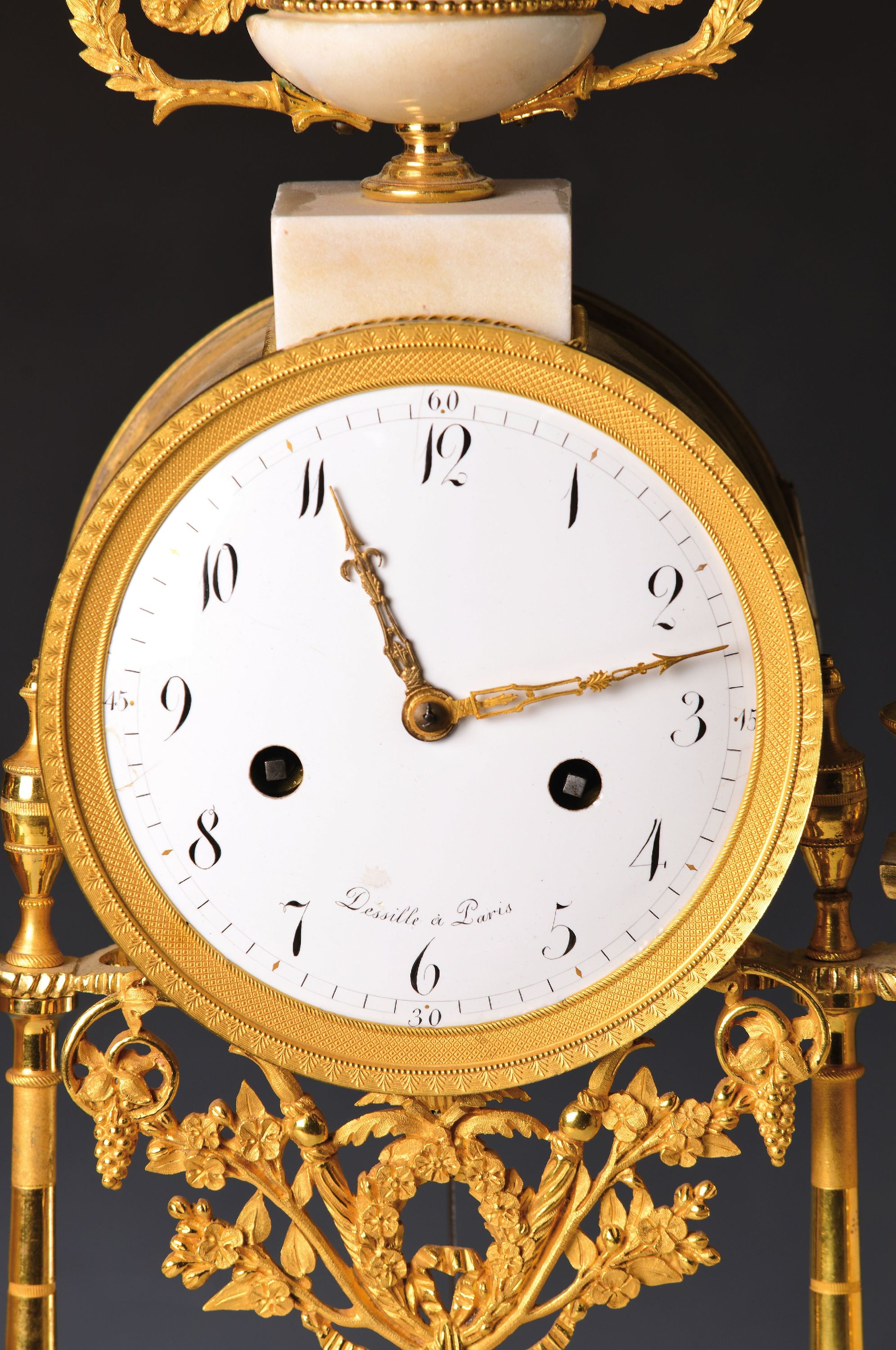 Detail c: Portaluhr, Dessille a Paris, um 1790, feuervergoldete Appliken auf weißem Marmor, Sockel mit reliefierten Putti, darauf zwei ovale Plinthen mit ...