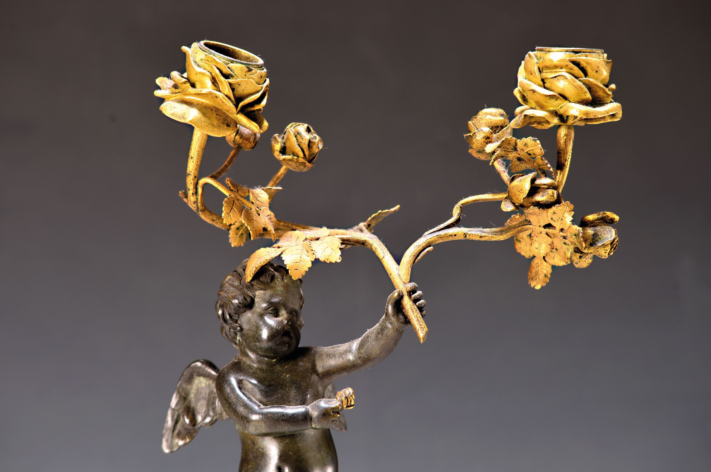 Detail a: Paar Bronzeleuchter, Frankreich, um 1770/80, Amoretten mit Rosen, je zwei Brennstellen, patiniert, z.T. vergoldet, Marmorpostamente in Form von ...