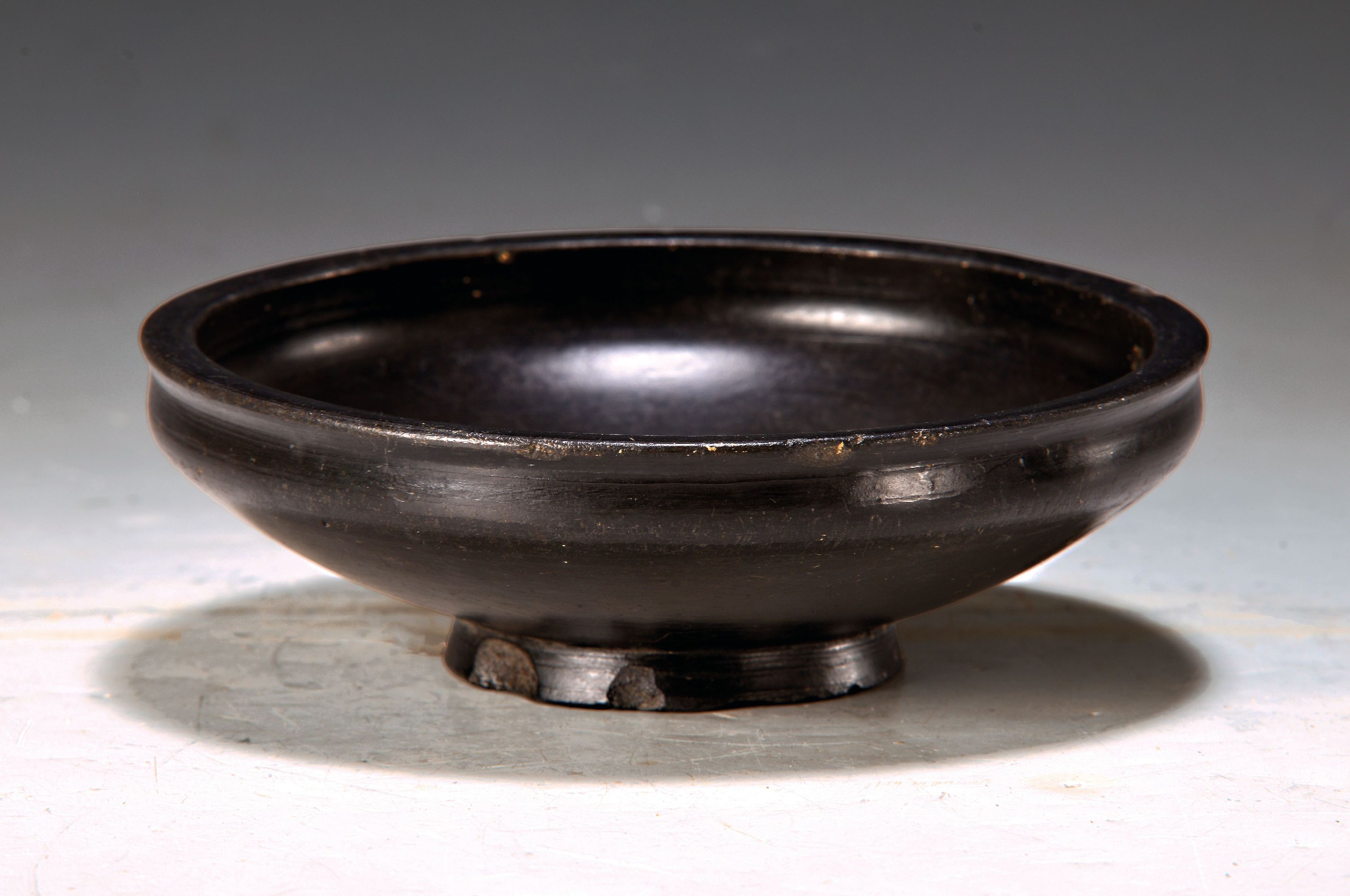 Etruskische Bucchero Schale, 5./6.Jh., schwarz gebrannte Keramik, mehrfach bestoßen, alte Durchbohrung, auf rundem Stand, D. 19 cm, Provenienz: ...