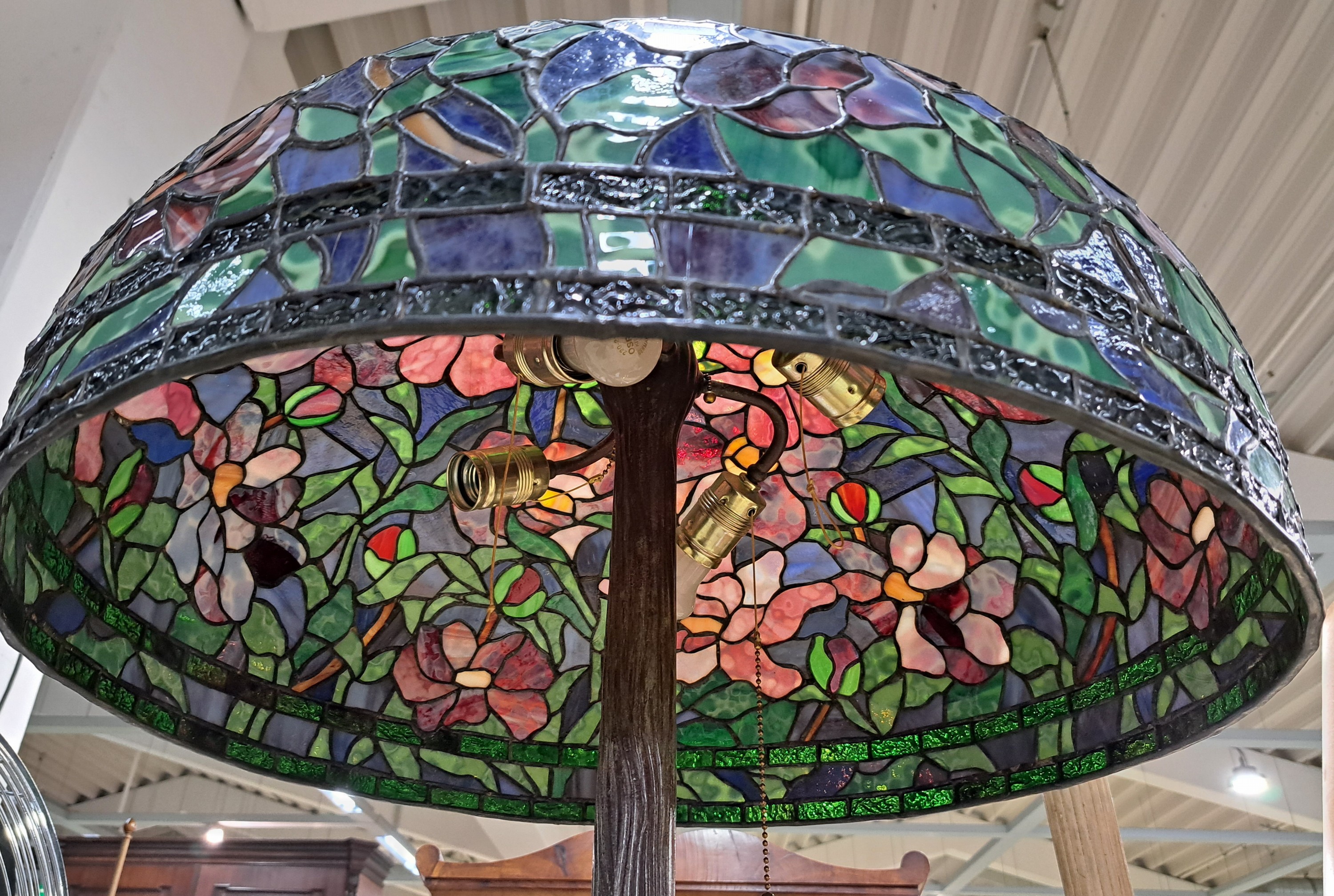Detail a: Stehlampe im Tiffanystil, wohl 80er Jahre, Bronzefuß in Form eines Baumstammes, patiniert, glockenförmiger Schirm mit buntem Mosaikglas, Blumen- ...