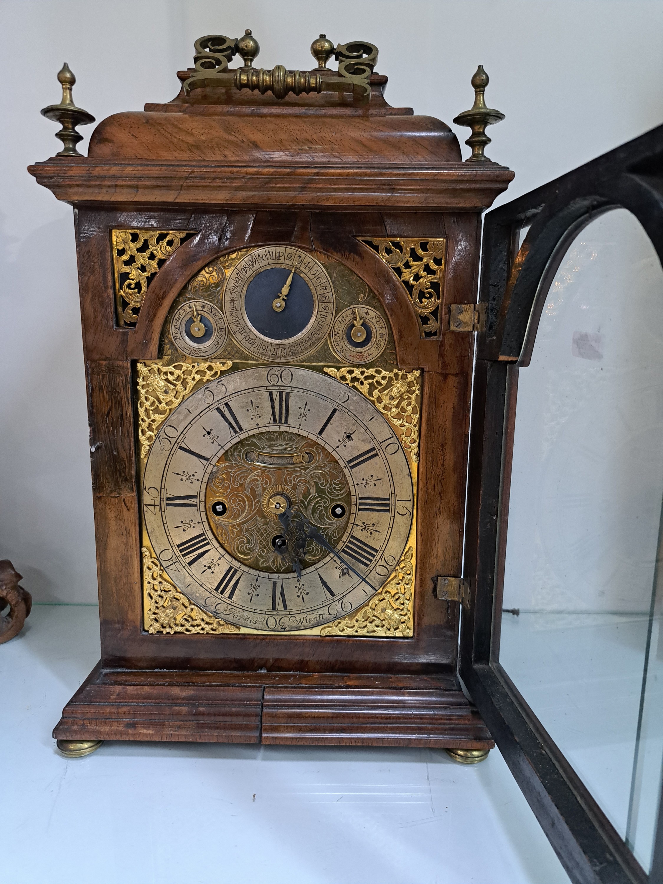 Detail b: Barockuhr, Förster in Wien, Ende 18. Jh., Nußbaumgehäuse, Sockelleiste spannungsrissig, allseitig verglast, Bogenzifferblatt Messing, im Arkus ...