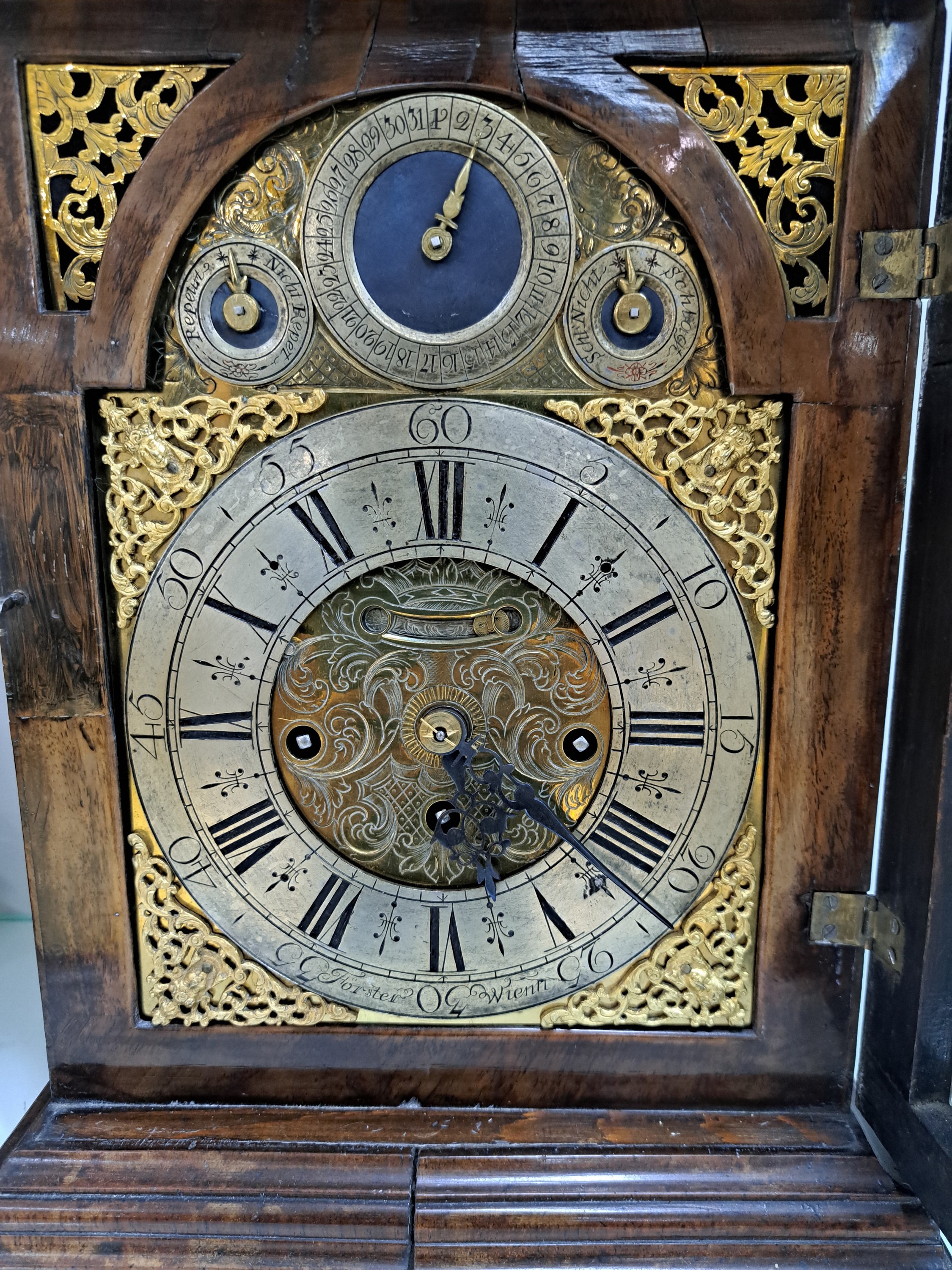 Detail c: Barockuhr, Förster in Wien, Ende 18. Jh., Nußbaumgehäuse, Sockelleiste spannungsrissig, allseitig verglast, Bogenzifferblatt Messing, im Arkus ...
