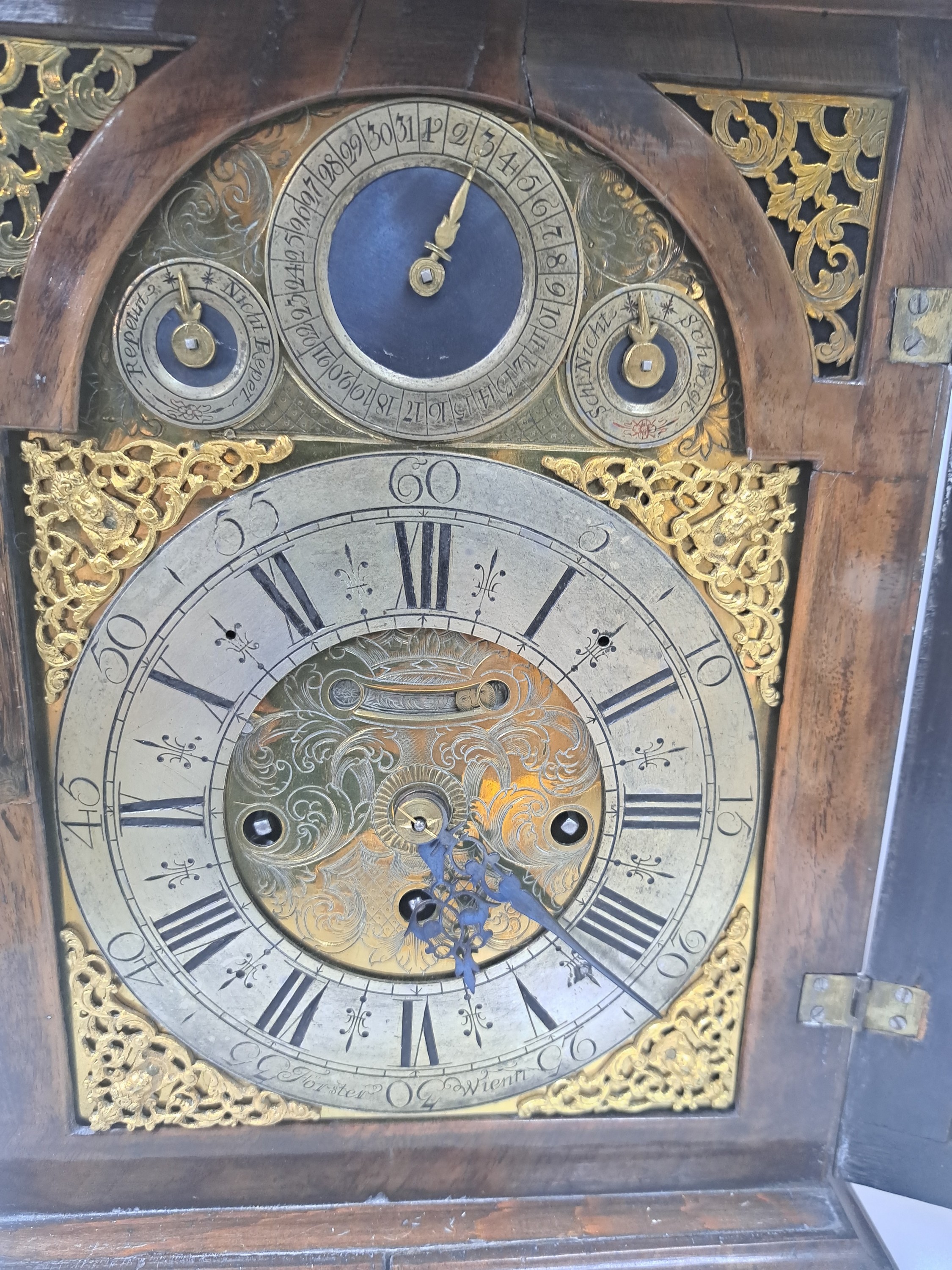 Detail i: Barockuhr, Förster in Wien, Ende 18. Jh., Nußbaumgehäuse, Sockelleiste spannungsrissig, allseitig verglast, Bogenzifferblatt Messing, im Arkus ...
