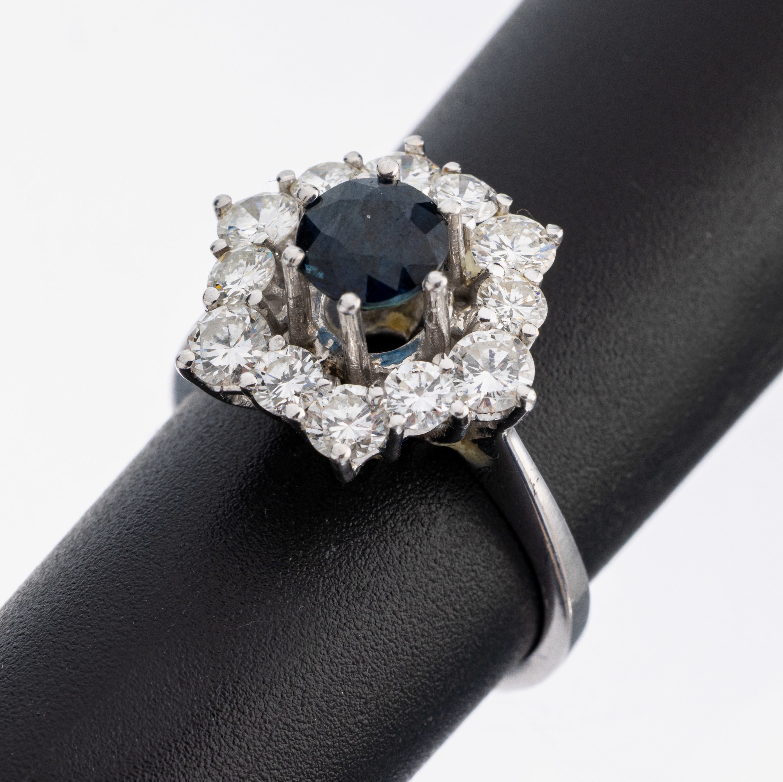 14 kt Gold Saphir-Brillant-Ring, WG 585/000, mittig erhaben gefasster rundfacett. Saphir ca. 1.0 ct, umgeben von 12 Brillanten zus. ca. 1.20 ct ...