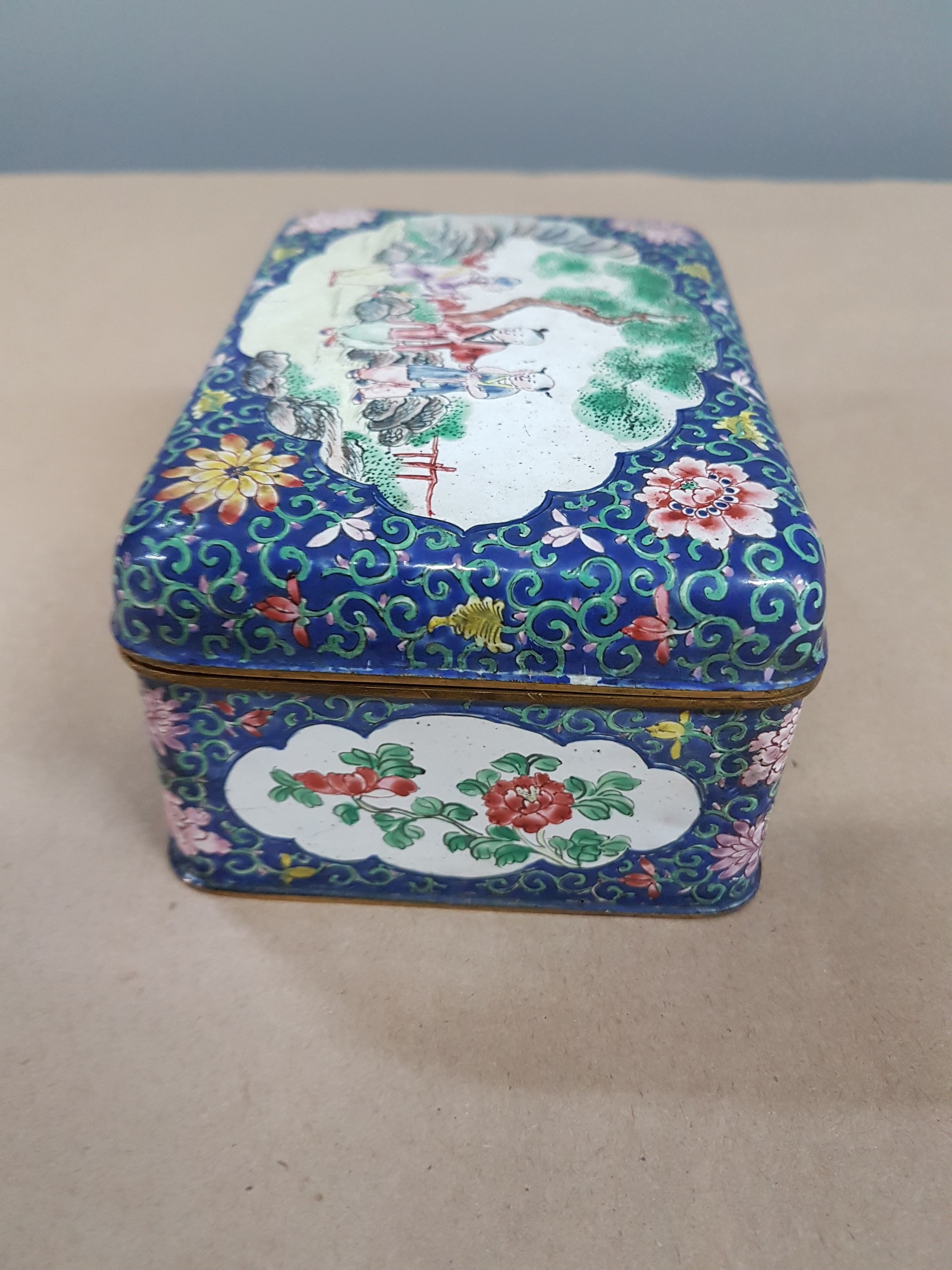 Detail c: Deckeldose, China, 20. Jh., Emailarbeit, 3 figürliche Szenen in Landschaft bemalt, zwei Kartuschen mit Blumenmalerei, ca. 6 x 12 x 9 cm