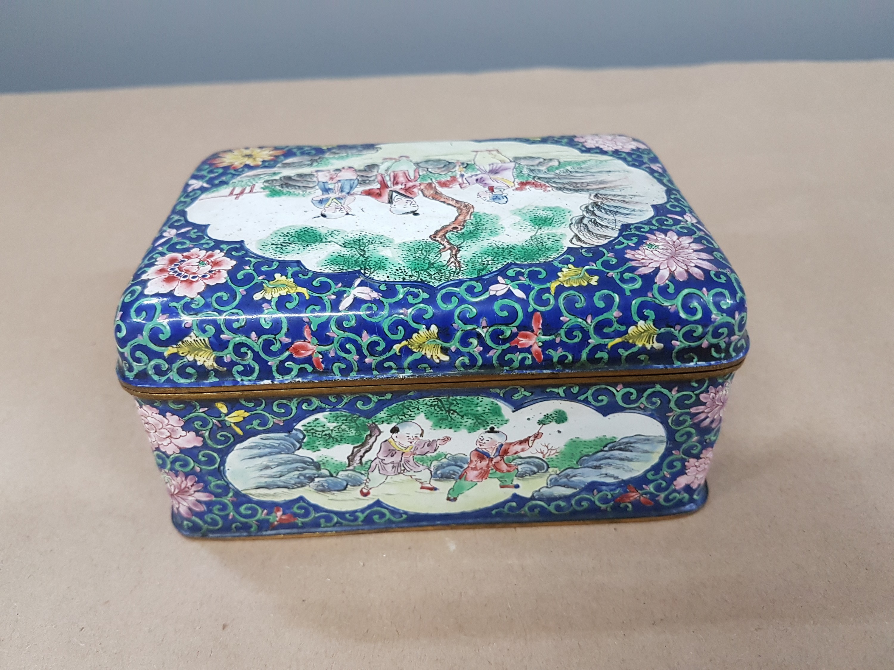 Detail d: Deckeldose, China, 20. Jh., Emailarbeit, 3 figürliche Szenen in Landschaft bemalt, zwei Kartuschen mit Blumenmalerei, ca. 6 x 12 x 9 cm