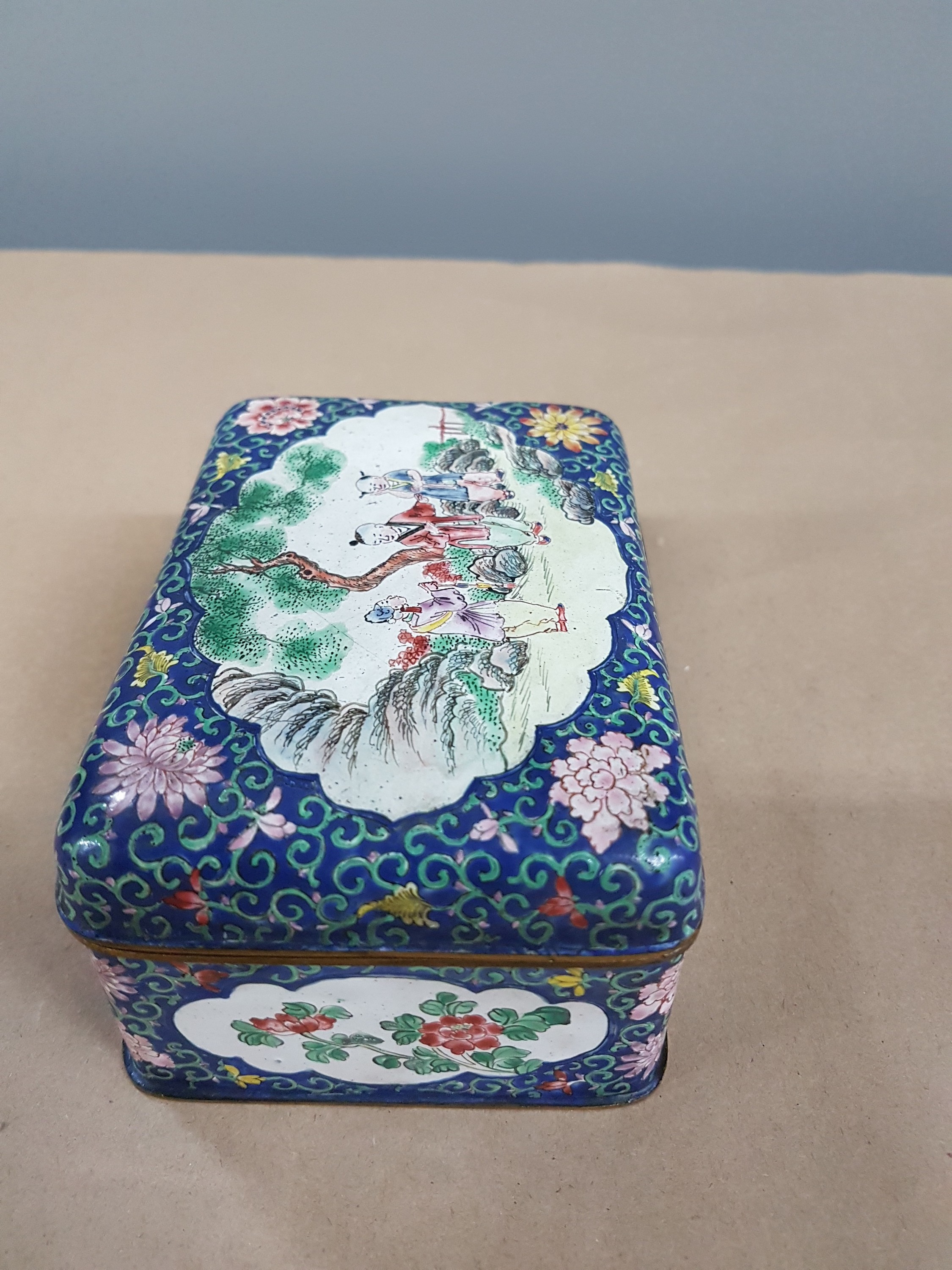 Detail e: Deckeldose, China, 20. Jh., Emailarbeit, 3 figürliche Szenen in Landschaft bemalt, zwei Kartuschen mit Blumenmalerei, ca. 6 x 12 x 9 cm