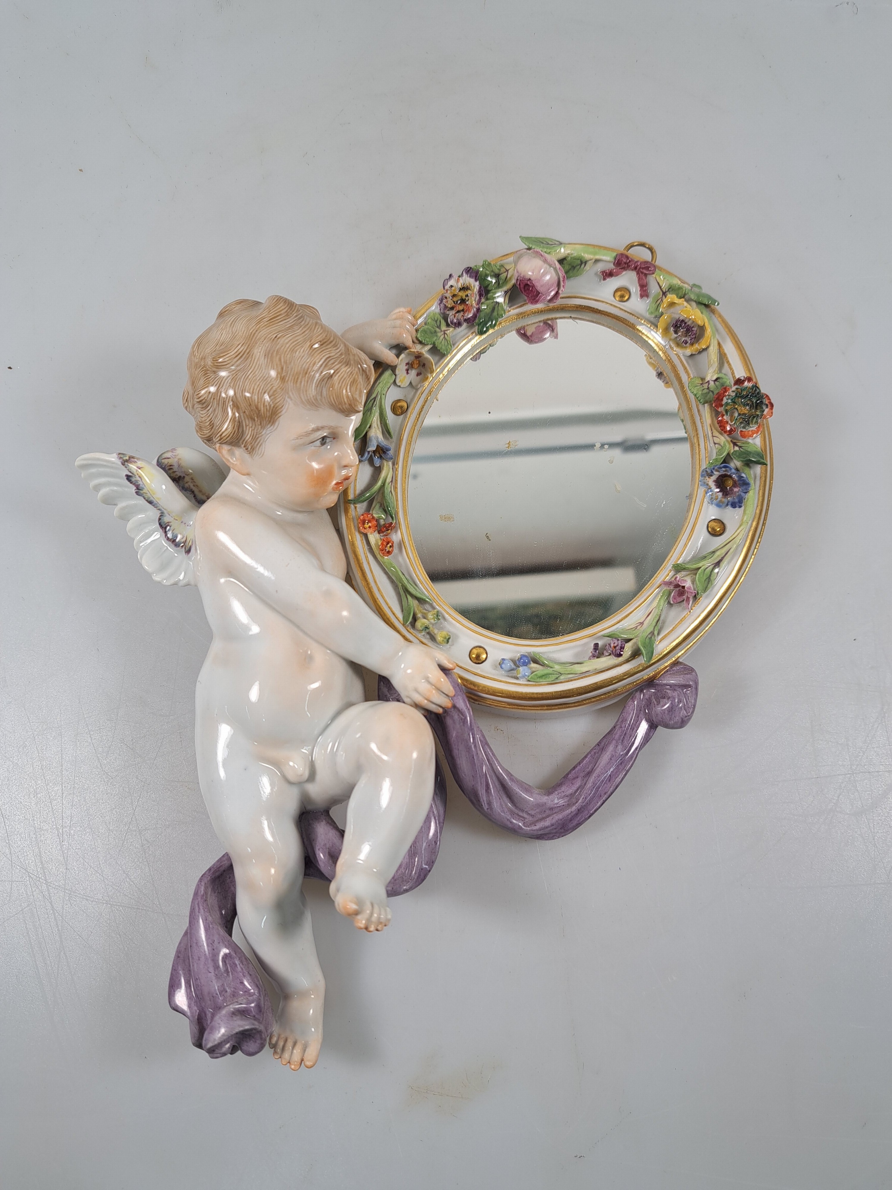 Detail a: Wandspiegel mit Amorette, Meissen um 1900, Porzellan, Amorette mit lilafarbener Schärpe hält eine ovalen Spiegel, applizierte Blüten, polychrom ...