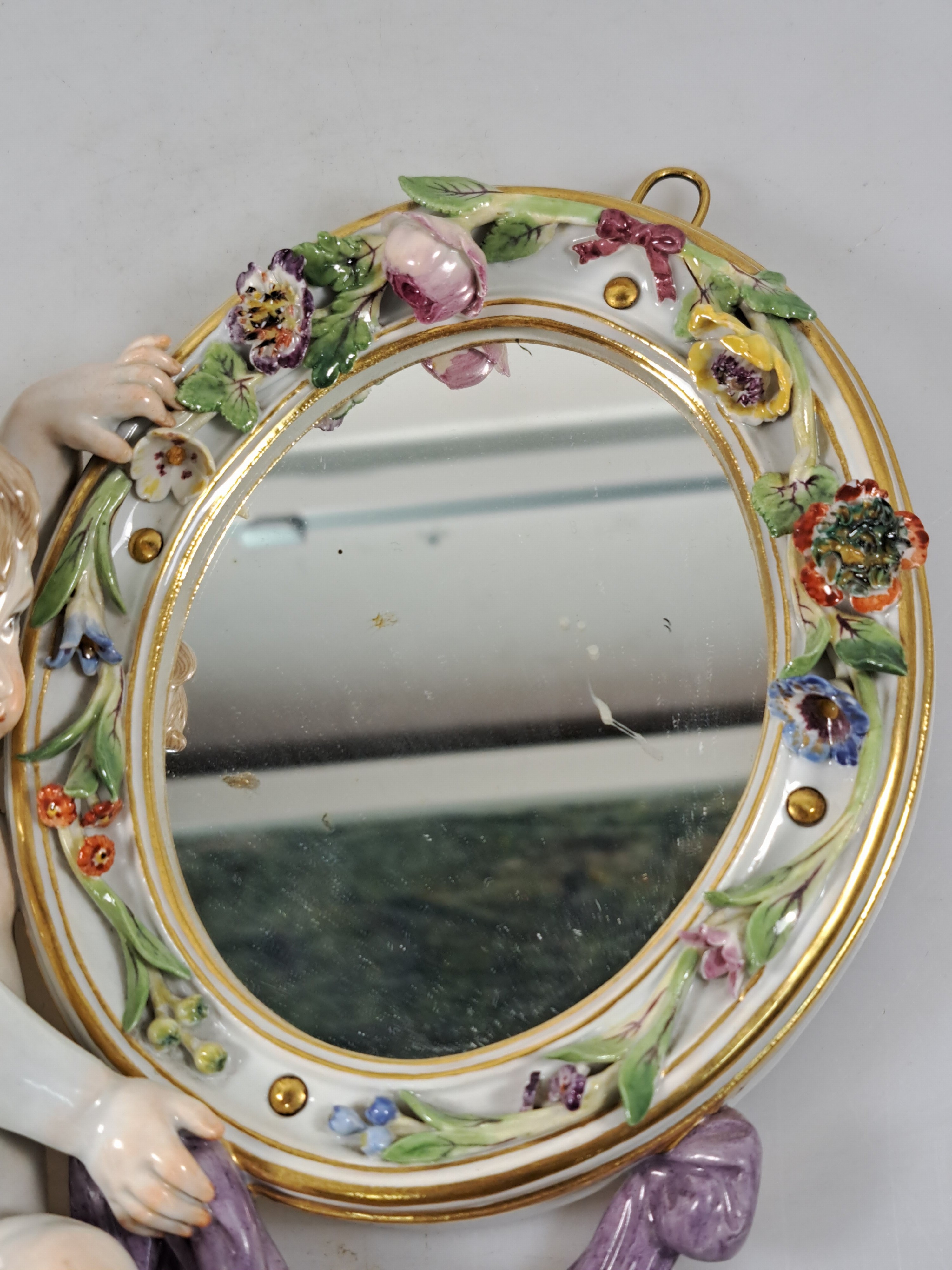 Detail b: Wandspiegel mit Amorette, Meissen um 1900, Porzellan, Amorette mit lilafarbener Schärpe hält eine ovalen Spiegel, applizierte Blüten, polychrom ...