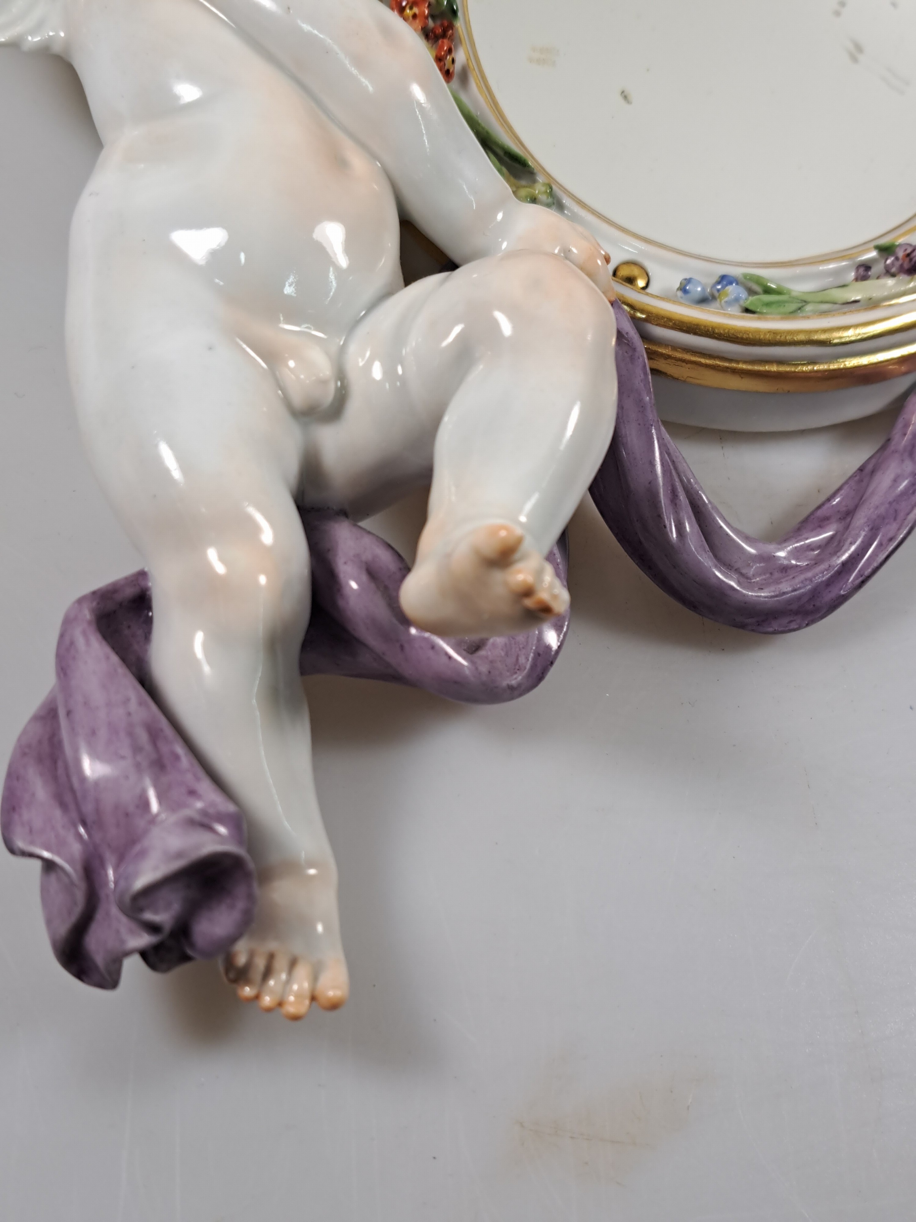 Detail d: Wandspiegel mit Amorette, Meissen um 1900, Porzellan, Amorette mit lilafarbener Schärpe hält eine ovalen Spiegel, applizierte Blüten, polychrom ...