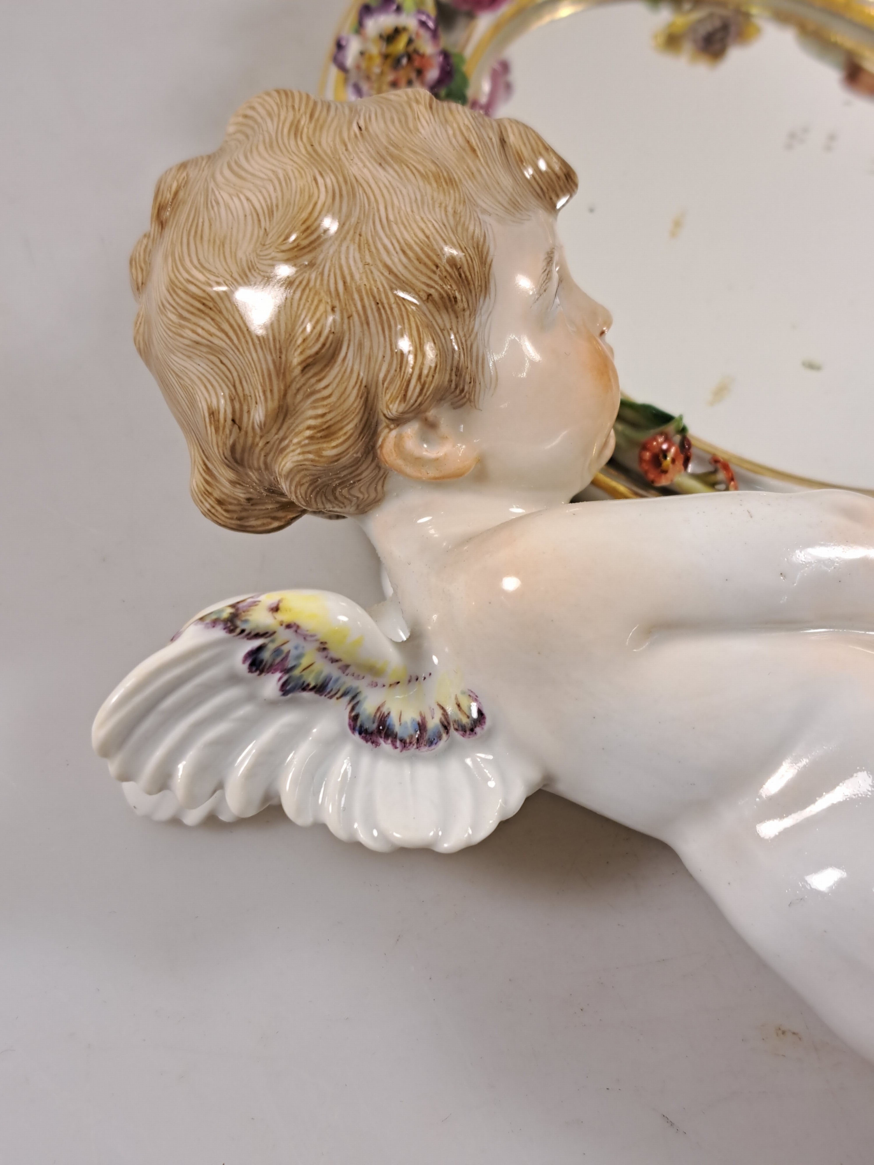 Detail e: Wandspiegel mit Amorette, Meissen um 1900, Porzellan, Amorette mit lilafarbener Schärpe hält eine ovalen Spiegel, applizierte Blüten, polychrom ...