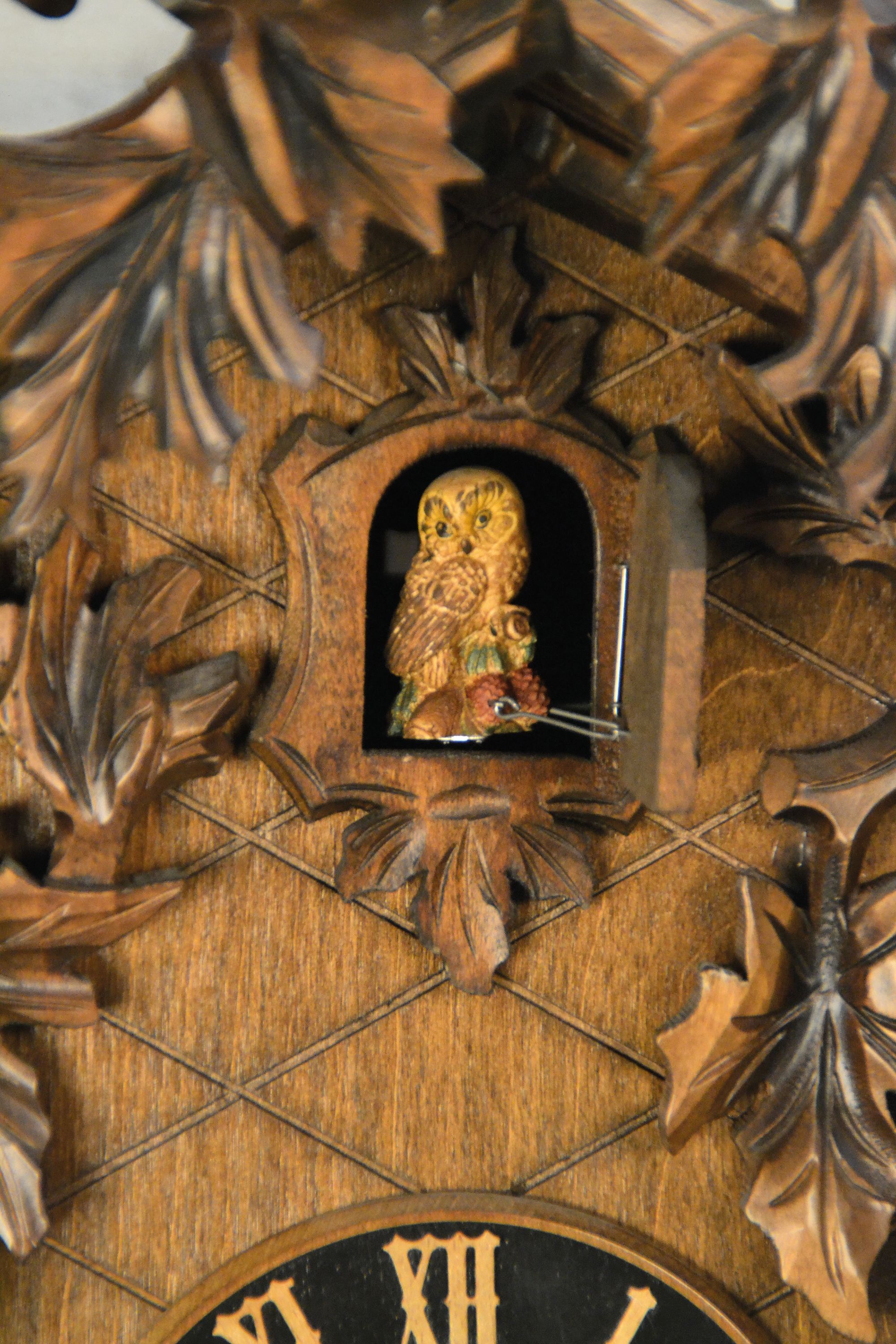 Detail a: Wanduhr mit Uhuruf und Musikspielwerk, Fa. Hönes, Titisee, um 1980, geschnitzte Front, mit plastischem Uhu und Blattwerk, orig. Aufsatz, seitliche ...