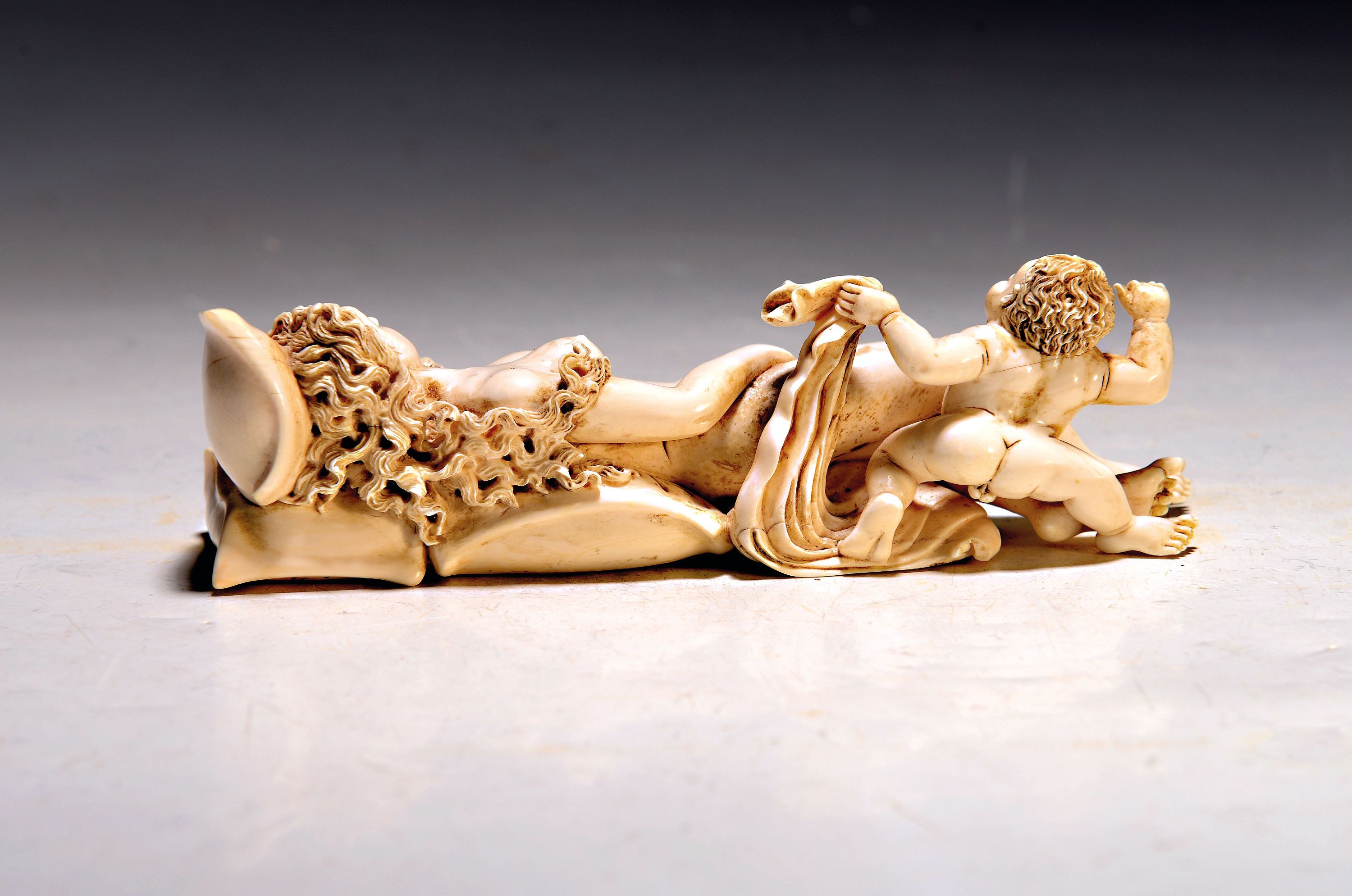 Detail a: Elfenbeinfigur, wohl flämisch, 17./18. Jh., liegende Venus mit Amor, die Göttin hat ihren Kopf auf einem Kissen liegen, mit einer Hand verdeckt sie ...