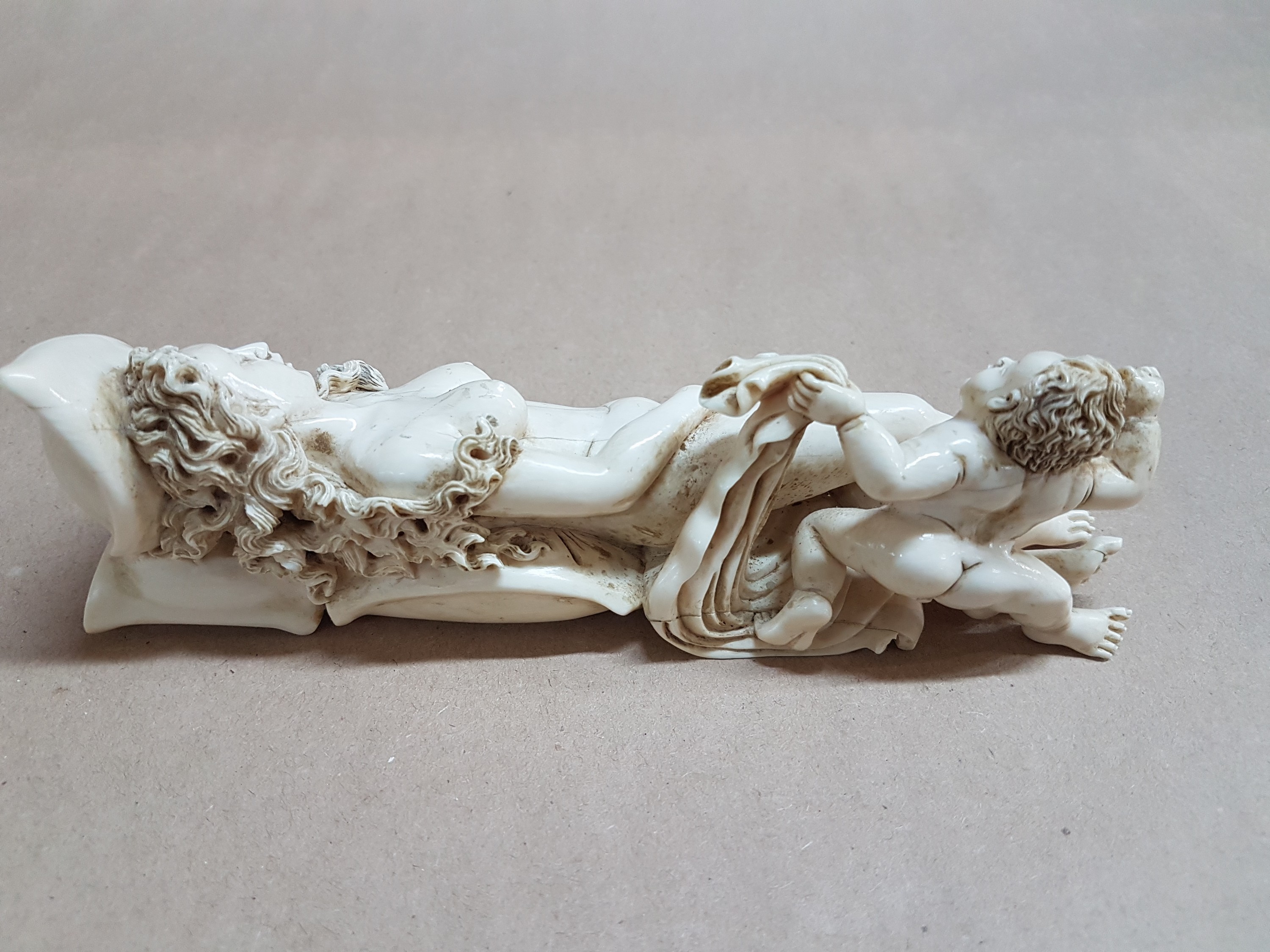 Detail i: Elfenbeinfigur, wohl flämisch, 17./18. Jh., liegende Venus mit Amor, die Göttin hat ihren Kopf auf einem Kissen liegen, mit einer Hand verdeckt sie ...