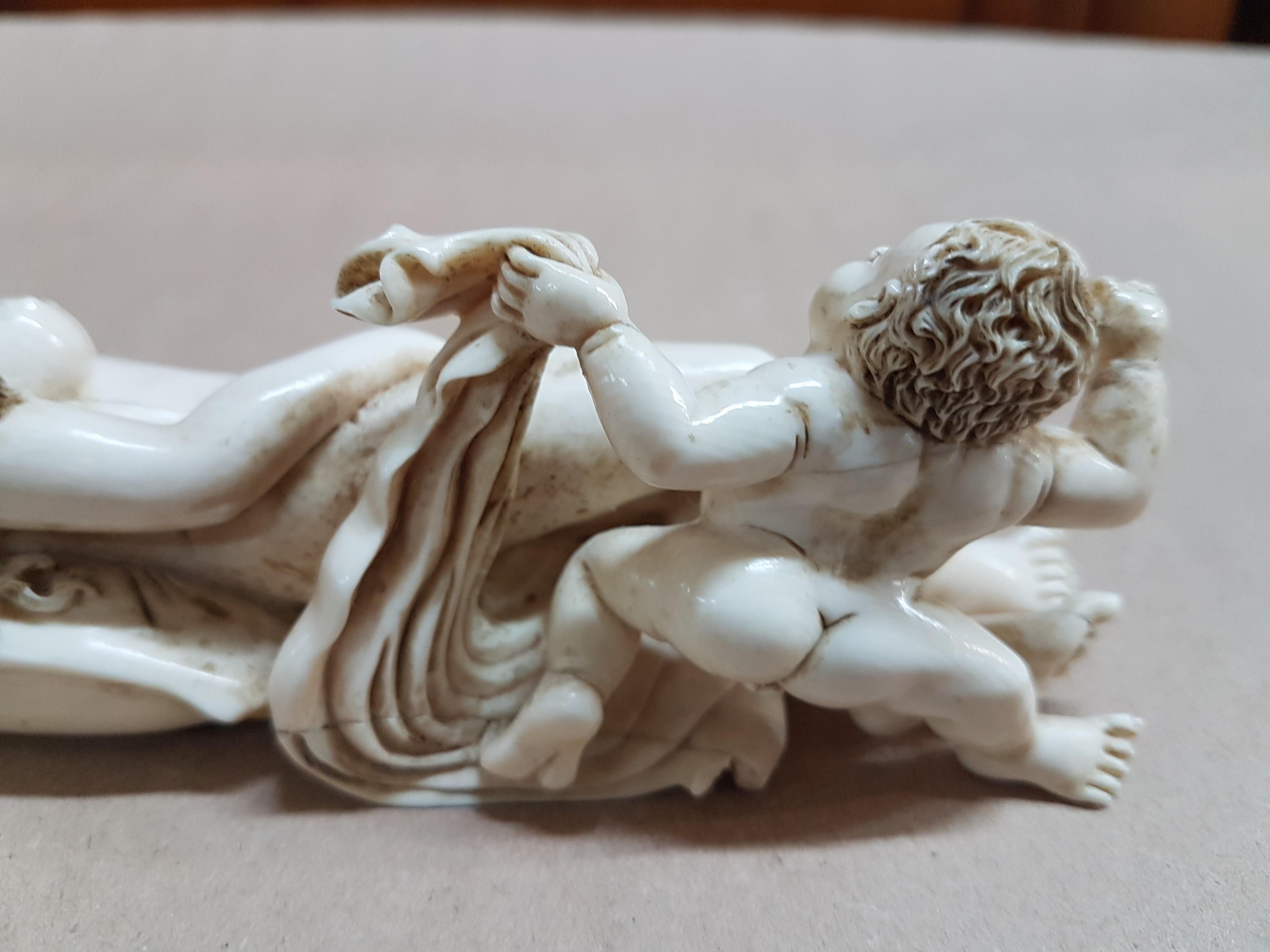 Detail k: Elfenbeinfigur, wohl flämisch, 17./18. Jh., liegende Venus mit Amor, die Göttin hat ihren Kopf auf einem Kissen liegen, mit einer Hand verdeckt sie ...