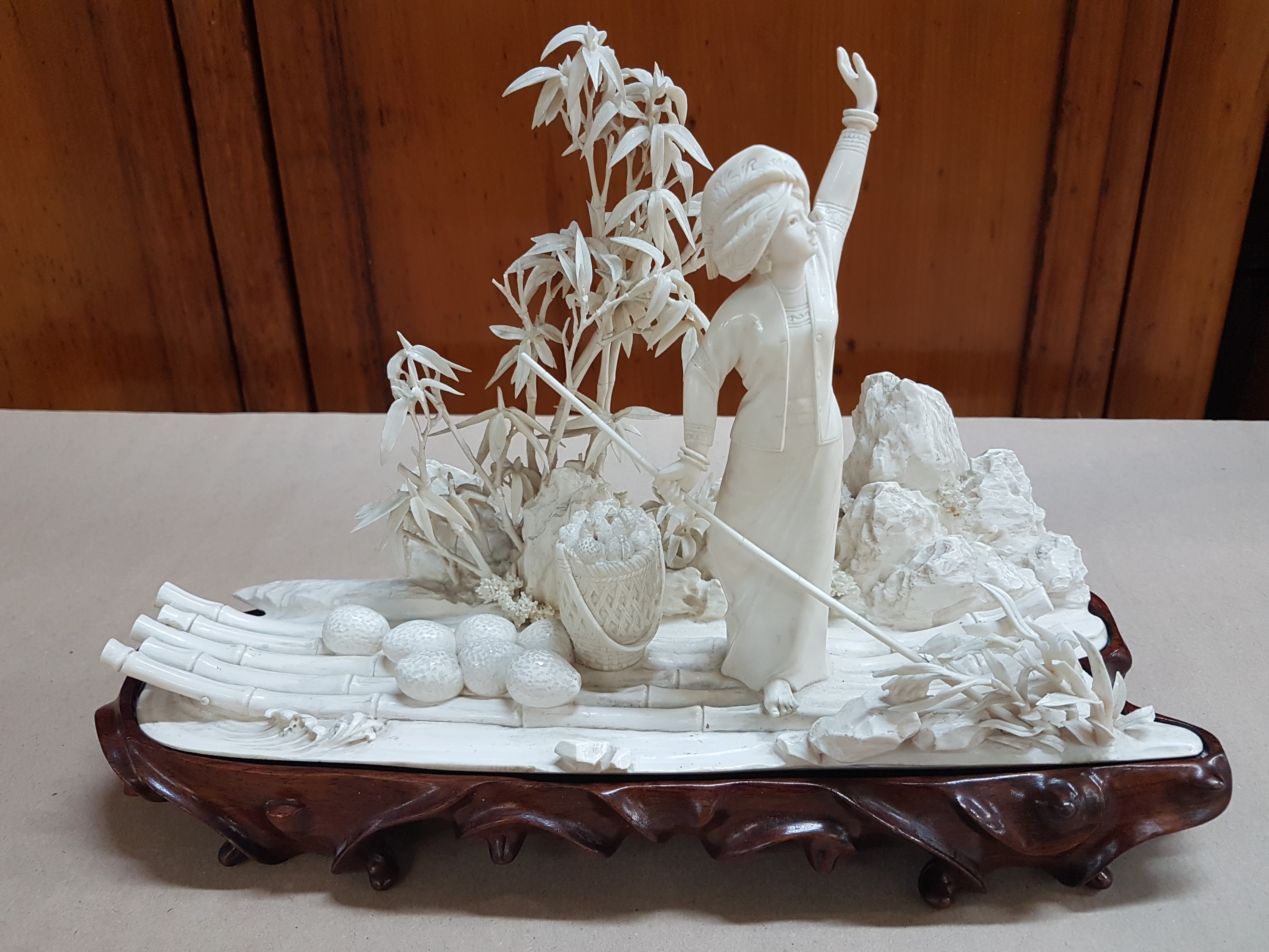 Detail d: Elfenbeinschnitzerei, China um 1900, Obstverkäuferin auf Floß, junge Frau mit erhobenem Arm und Stange, dahinter felsige Landschaft mit Bambus, ...