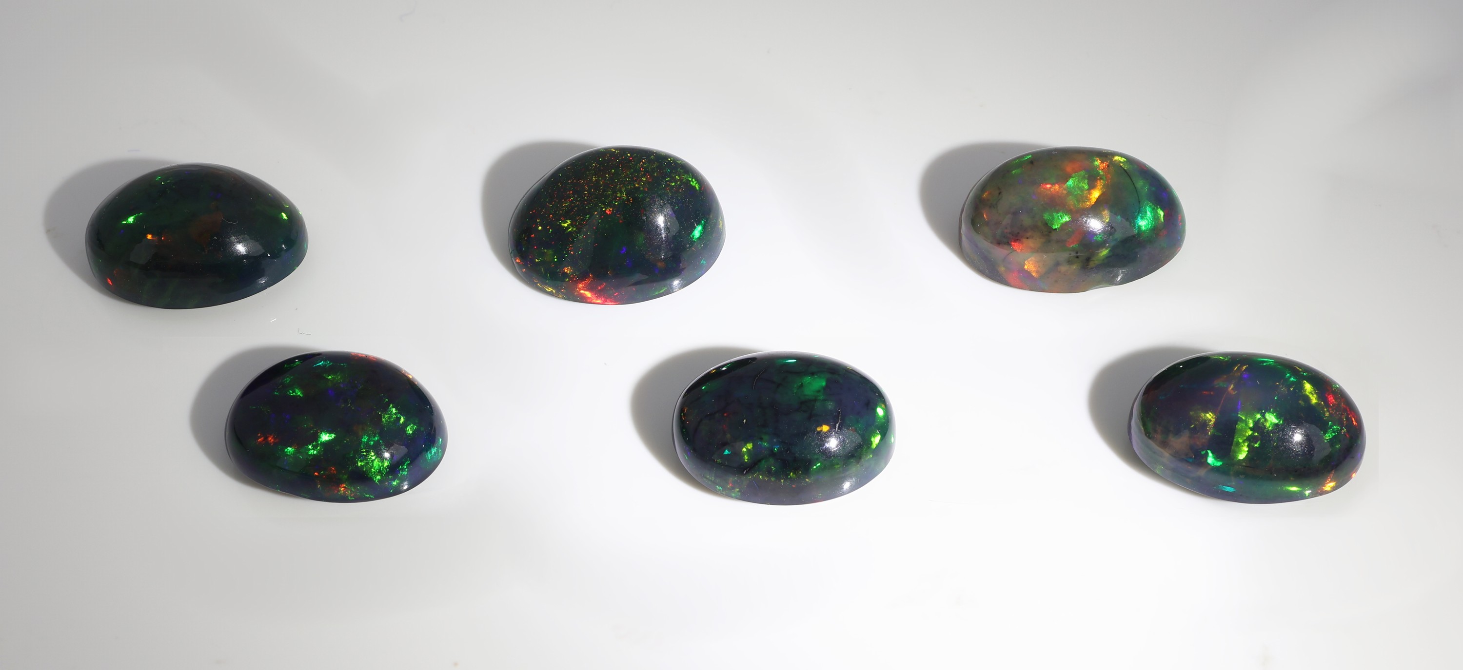 Detail a: Lot 6 lose schwarze Opale, zus. ca. 25.49 ct, ovale Cabochons in versch. Größen, intensives Farbspiel in Grün, Rot und Blau