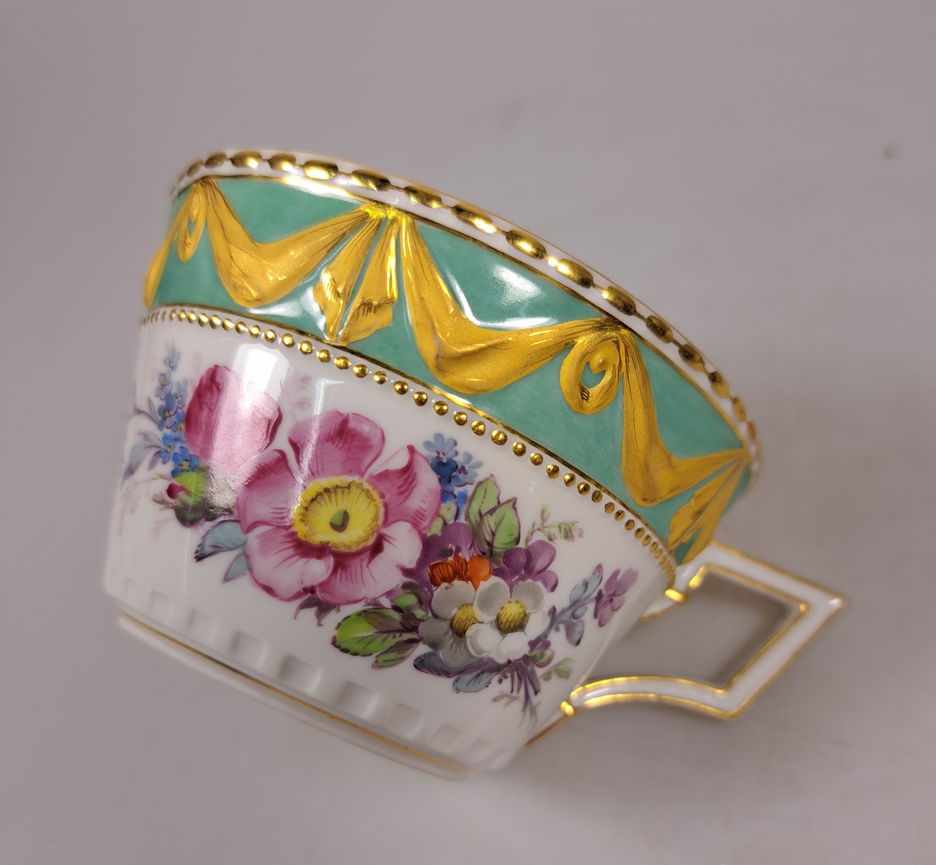 Detail d: Tasse mit Untertasse, KPM Berlin, Modell Kurland, Rand türkisfarben mit Matt- und Glanzvergoldung, bunte Blumenmalerei mit Insekten, H. ca. 5cm