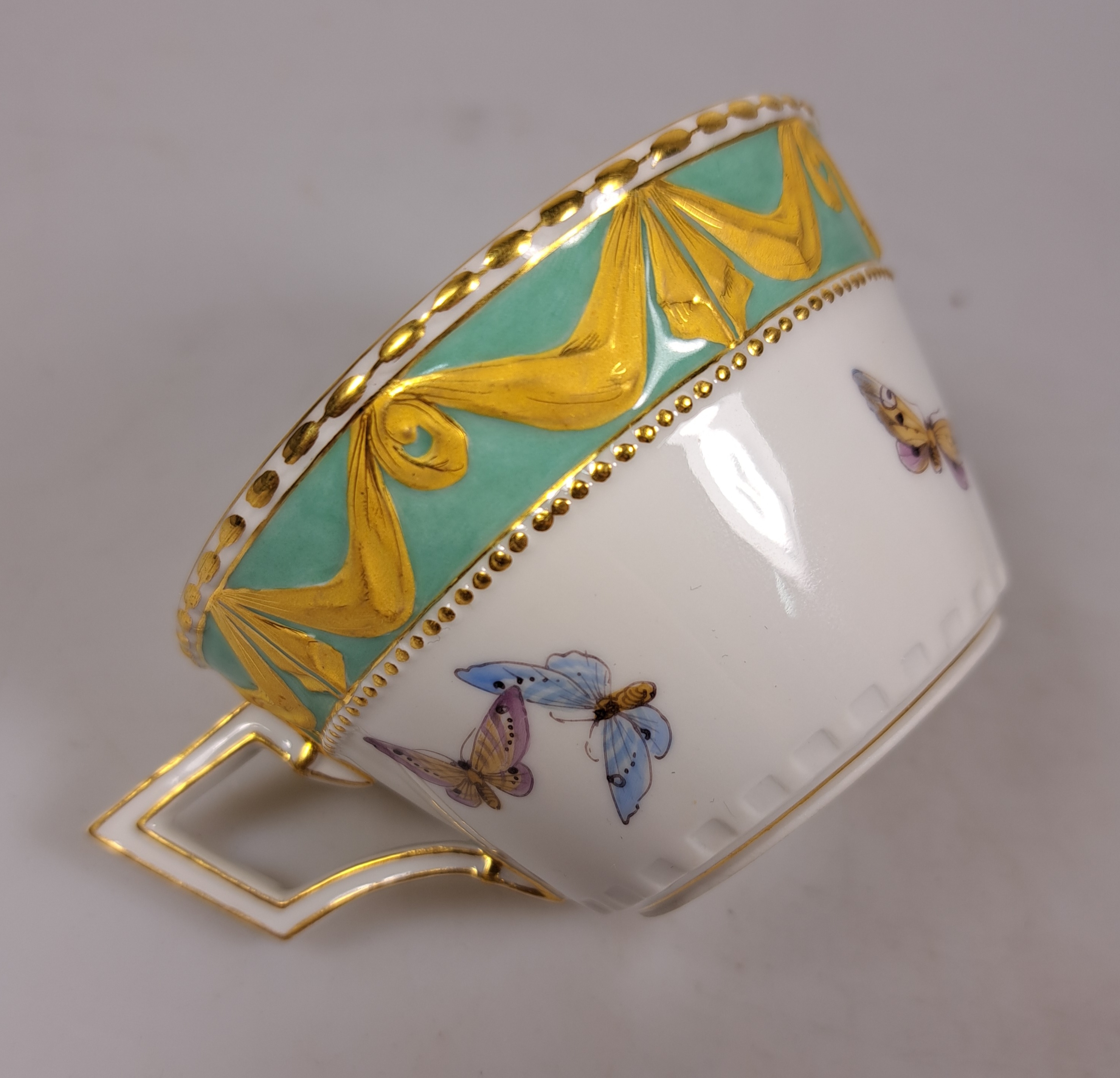 Detail e: Tasse mit Untertasse, KPM Berlin, Modell Kurland, Rand türkisfarben mit Matt- und Glanzvergoldung, bunte Blumenmalerei mit Insekten, H. ca. 5cm