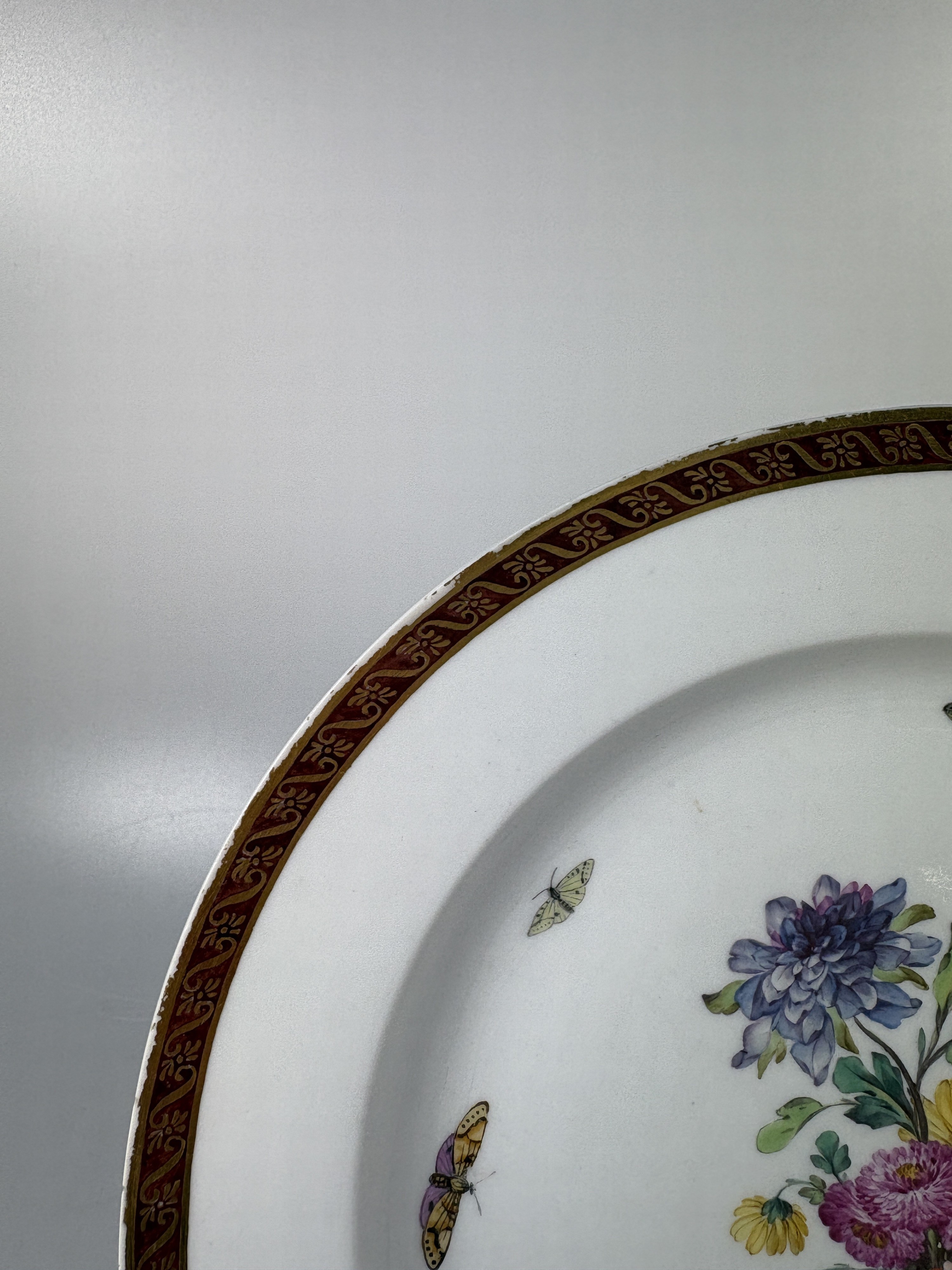 Detail f: Fünf Teller, KPM Berlin, Porzellan, vier davon um 1780, bordeauxfarbener Rand mit Goldstaffage, mittig Blumenbukettmalerei mit Schmetterlingen, D. ...