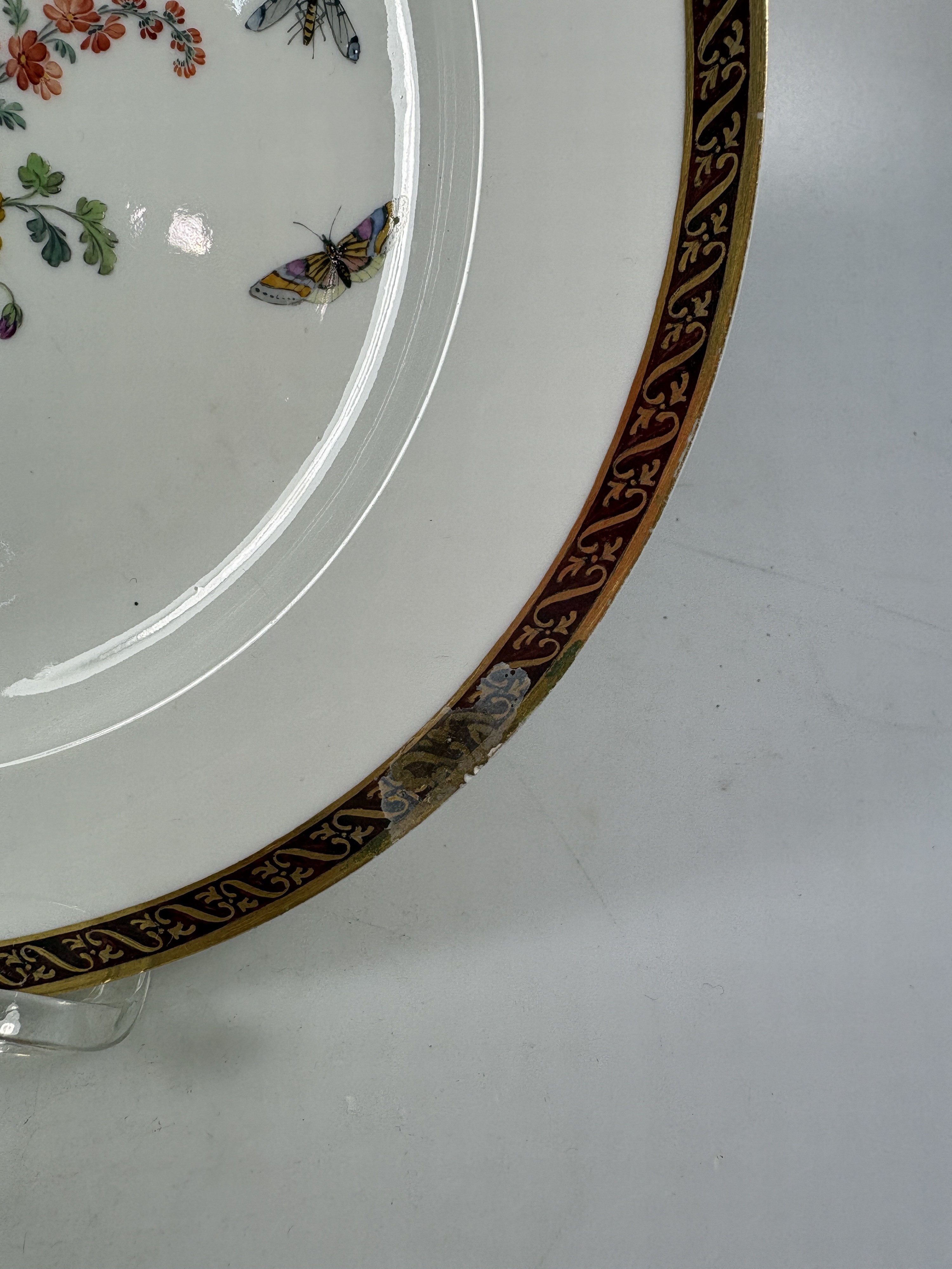 Detail i: Fünf Teller, KPM Berlin, Porzellan, vier davon um 1780, bordeauxfarbener Rand mit Goldstaffage, mittig Blumenbukettmalerei mit Schmetterlingen, D. ...
