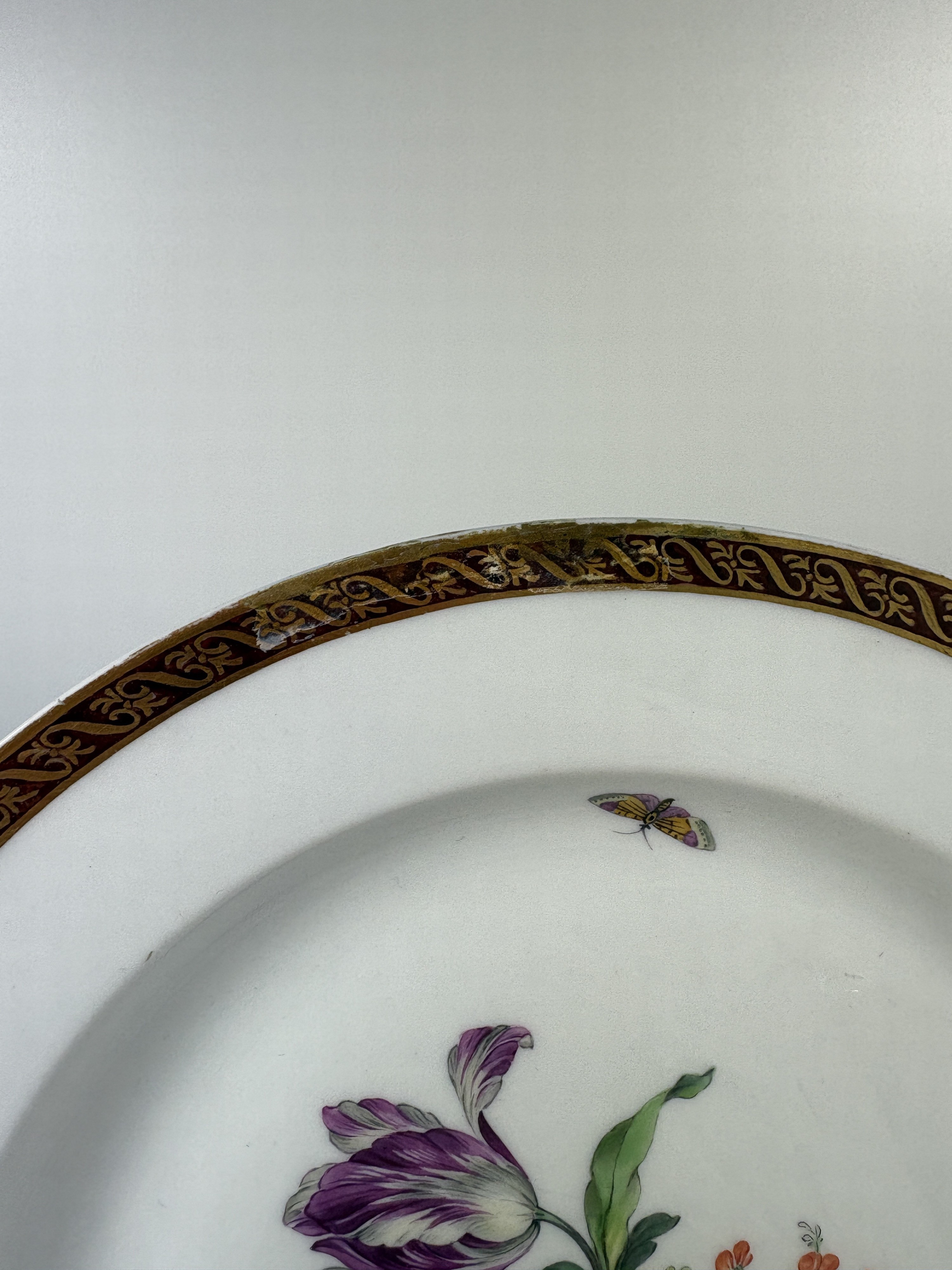 Detail k: Fünf Teller, KPM Berlin, Porzellan, vier davon um 1780, bordeauxfarbener Rand mit Goldstaffage, mittig Blumenbukettmalerei mit Schmetterlingen, D. ...