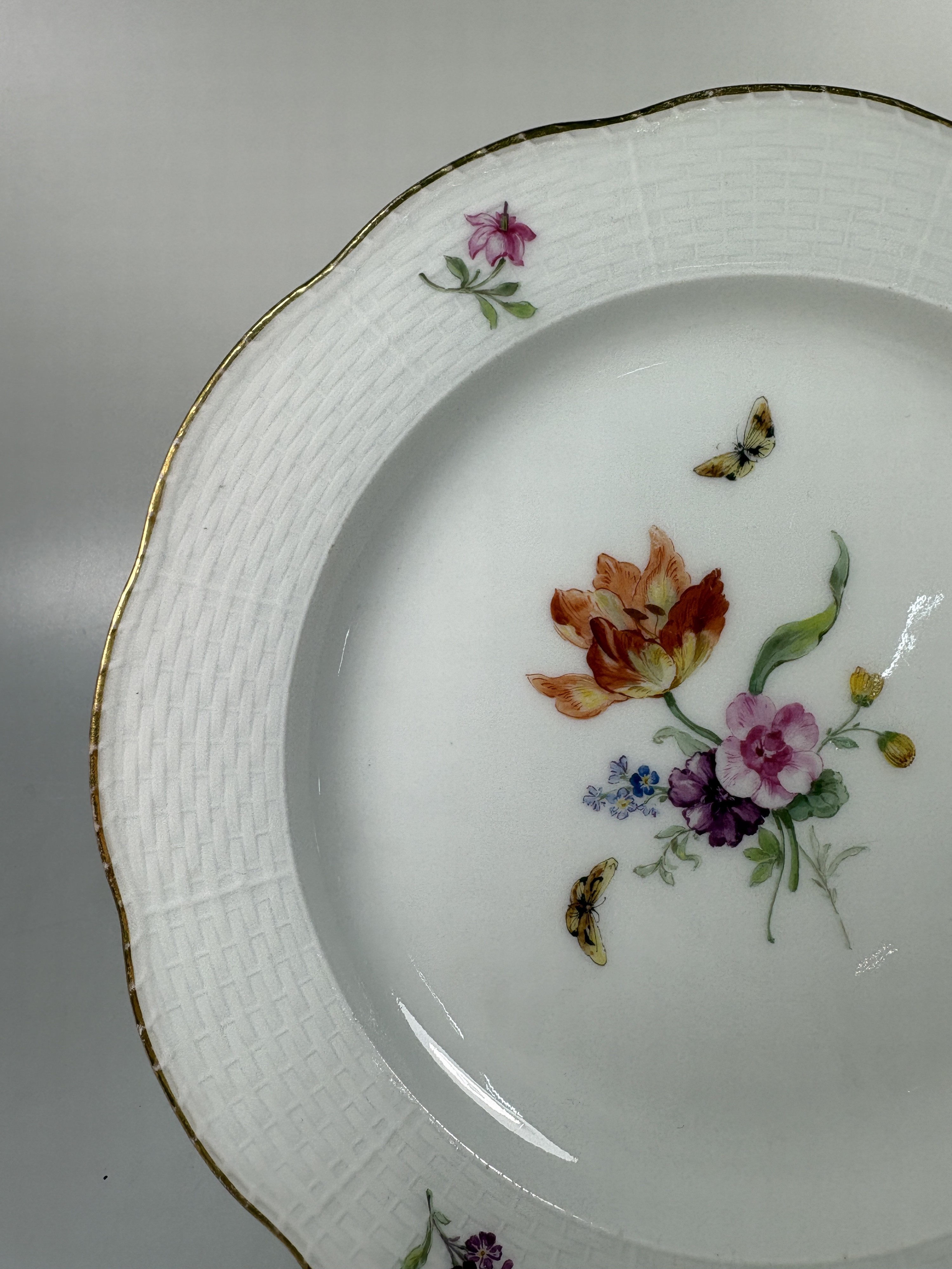 Detail n: Fünf Teller, KPM Berlin, Porzellan, vier davon um 1780, bordeauxfarbener Rand mit Goldstaffage, mittig Blumenbukettmalerei mit Schmetterlingen, D. ...