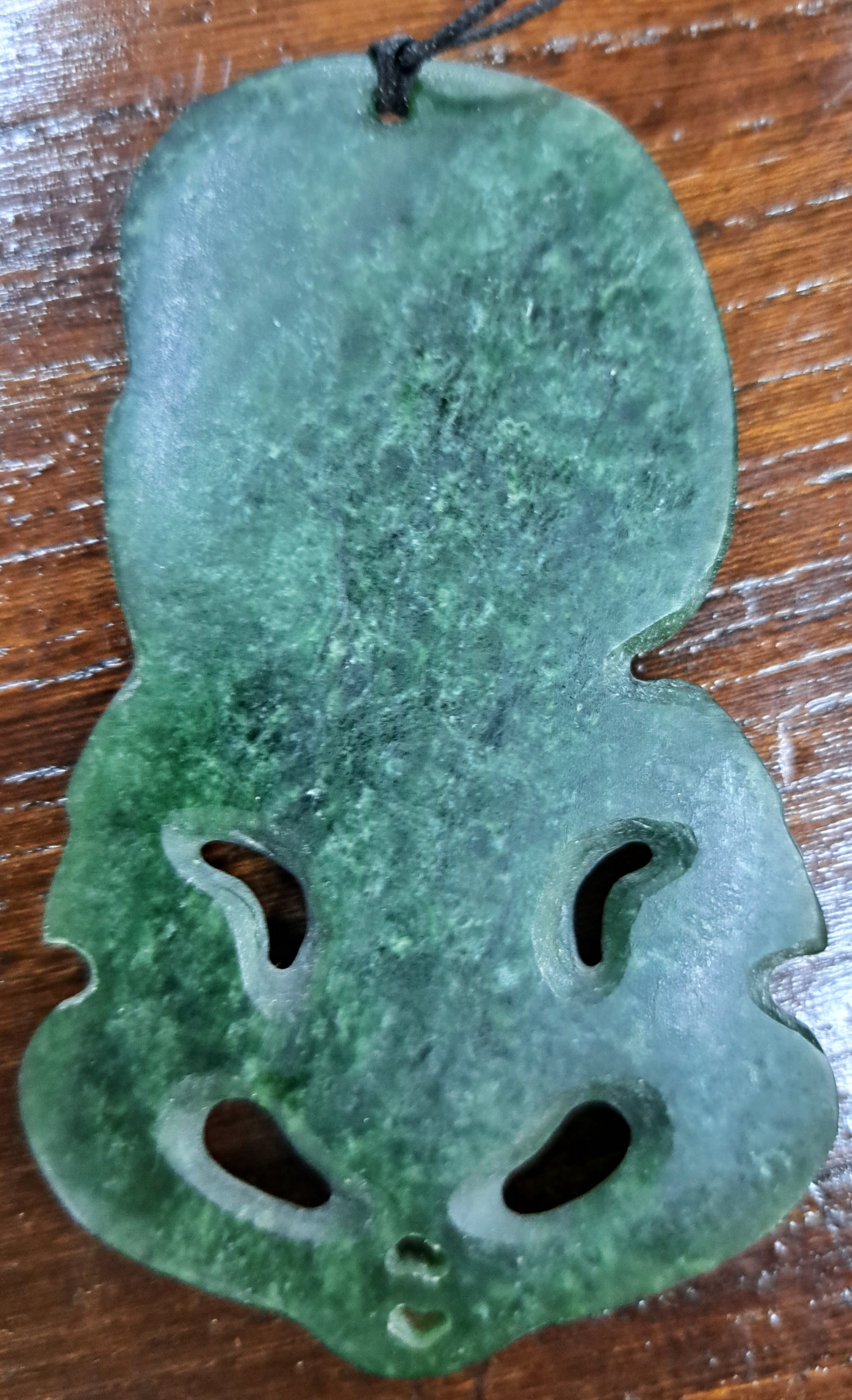 Detail b: Hei Tiki, Amulett der Maori, Neuseeland, Nephrit, sog. Greenstone, geschnitzt und geritzt, 9x5,5 cm, mit Lederband