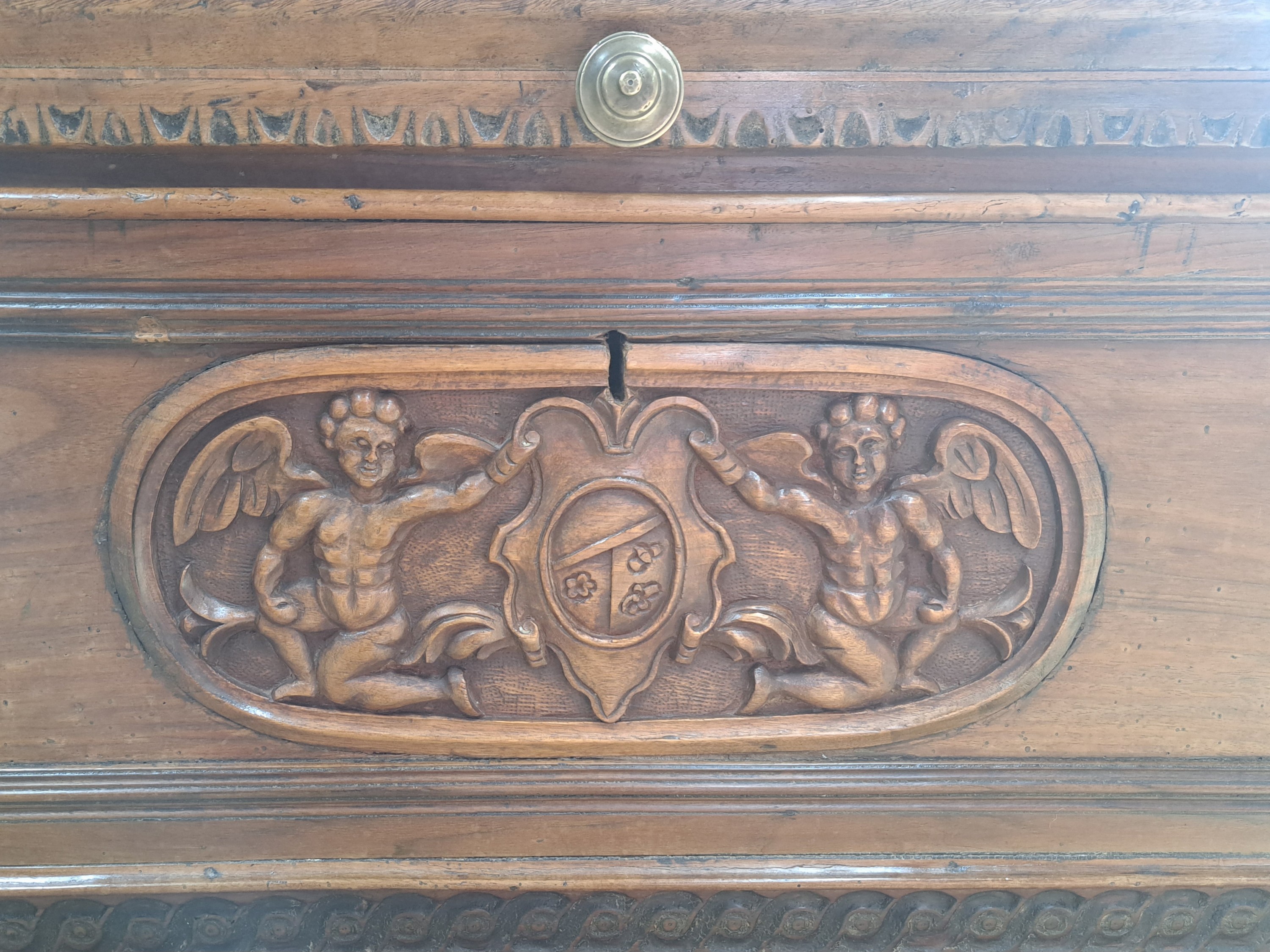 Detail b: Renaissance Truhe, Italien, um 1600, Nußbaummassiv, Front mit Reliefschnitzereien, Darstellung mit geflügelten Putto und Wappen, orig. Sockel, ...