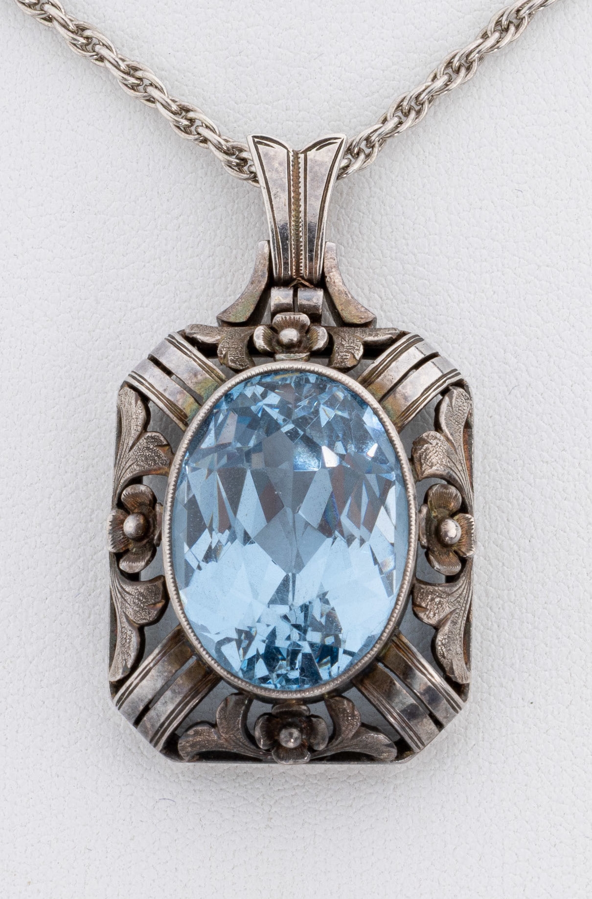 Detail a: Farbstein-Anhänger, 1920er-30er Jahre, 835er Silber, ovalfacett. blauer synth. Spinell, Fassung durchbrochen mit Blüten und Blättern, an Kette, ...